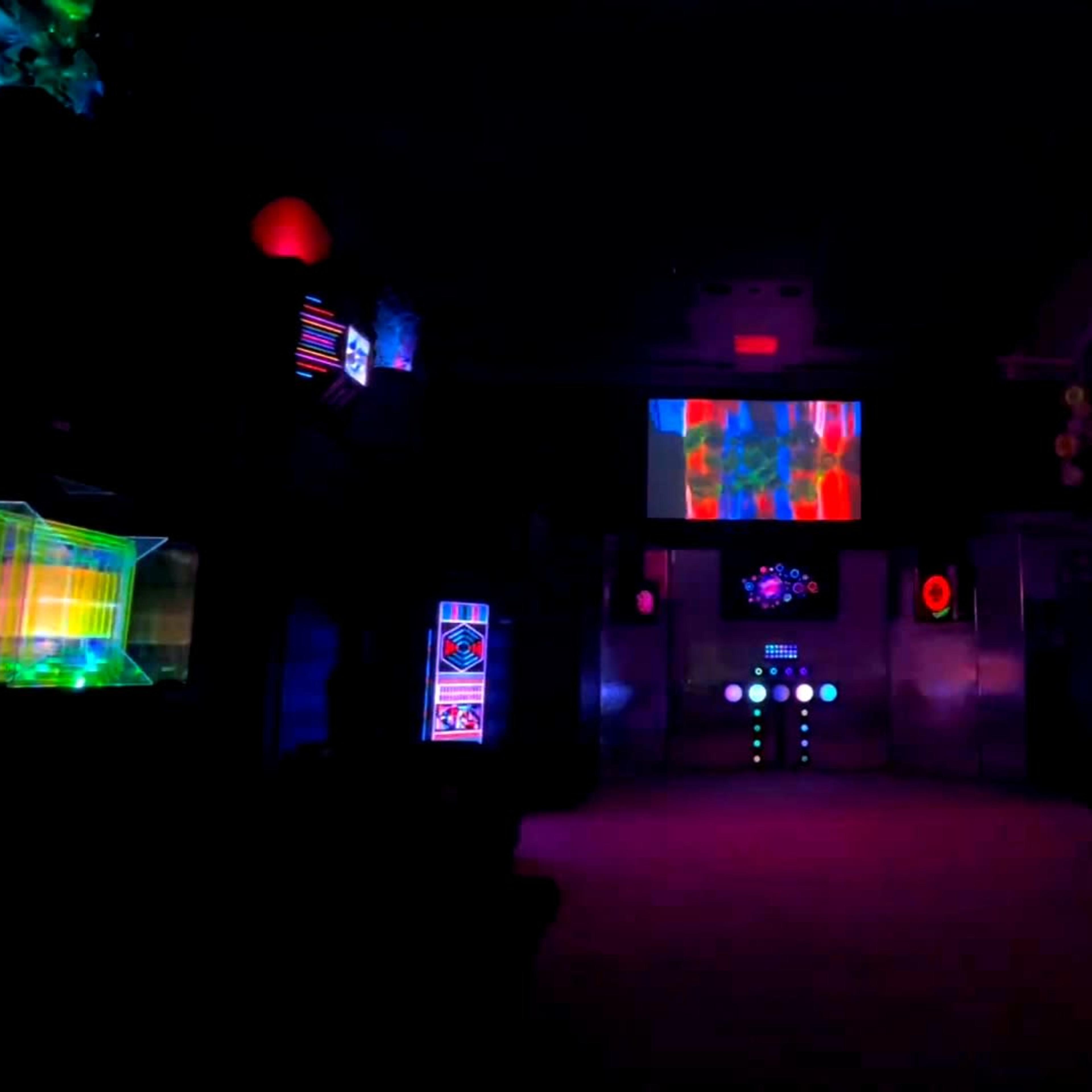 The scene features a dark room illuminated by colorful lights and displays, showcasing various futuristic panels and screens.