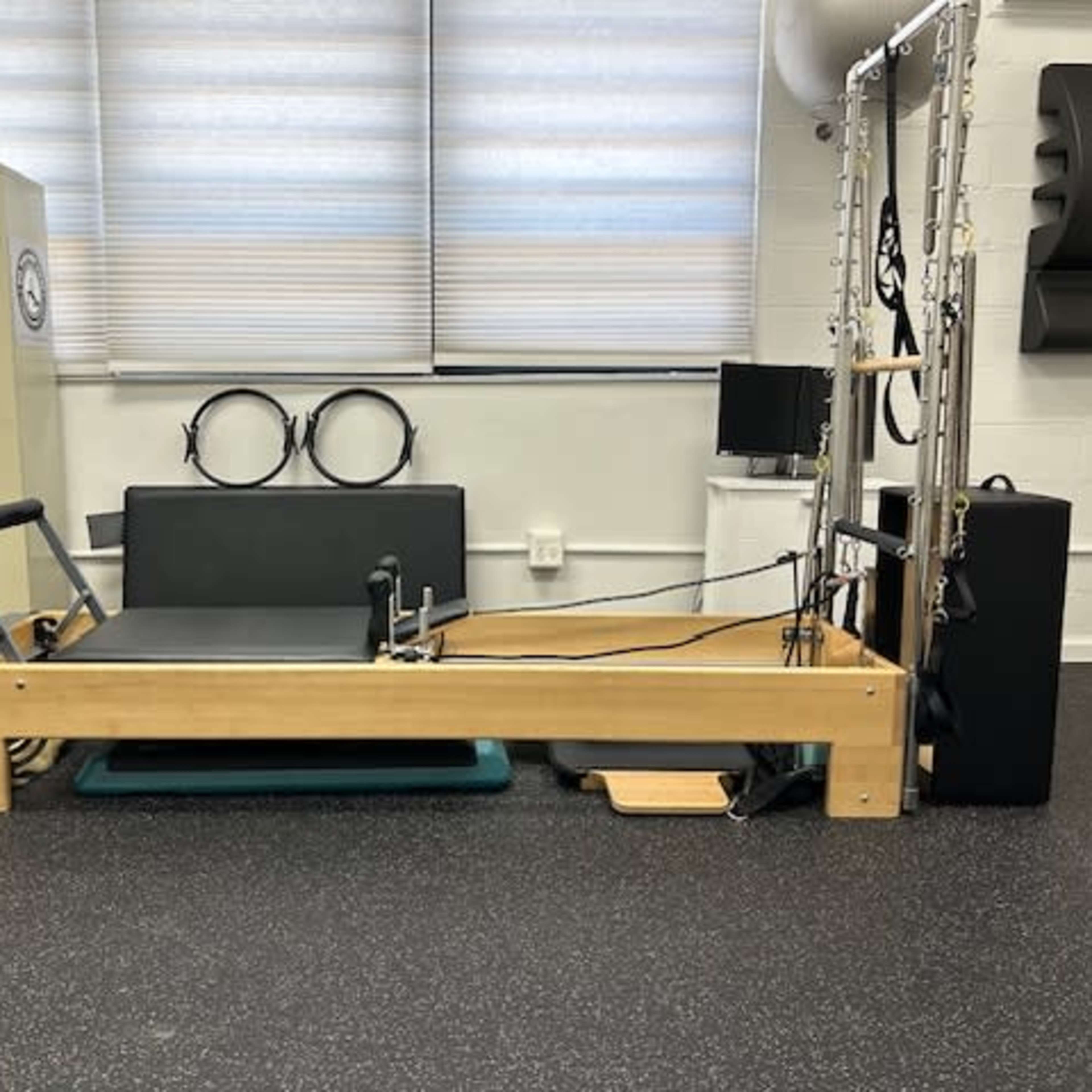 A Pilates reformer machine positioned in a studio with exercise accessories, such as rings and a television.