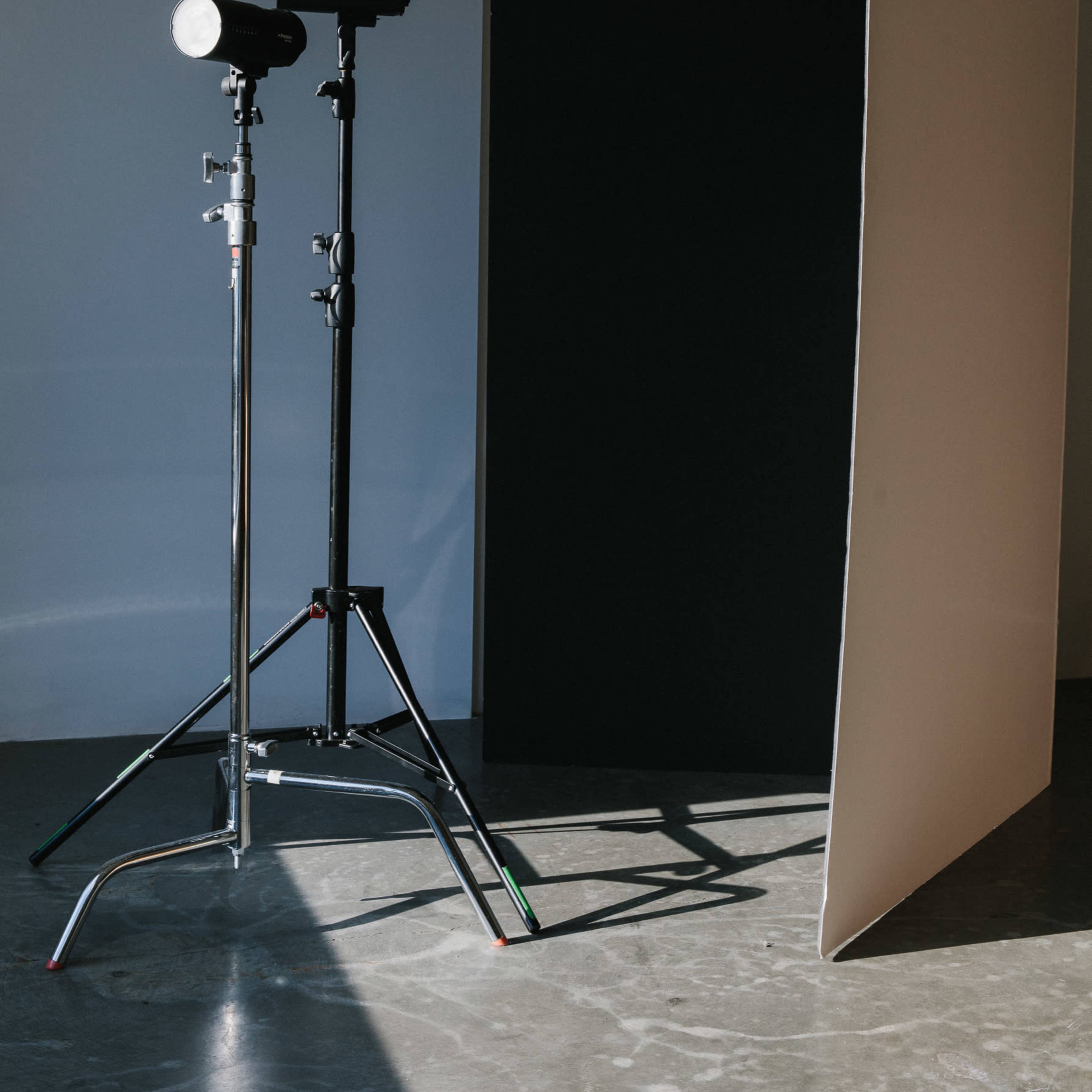A photography setup features two light stands with a softbox and a black backdrop positioned against a wall on a concrete floor.