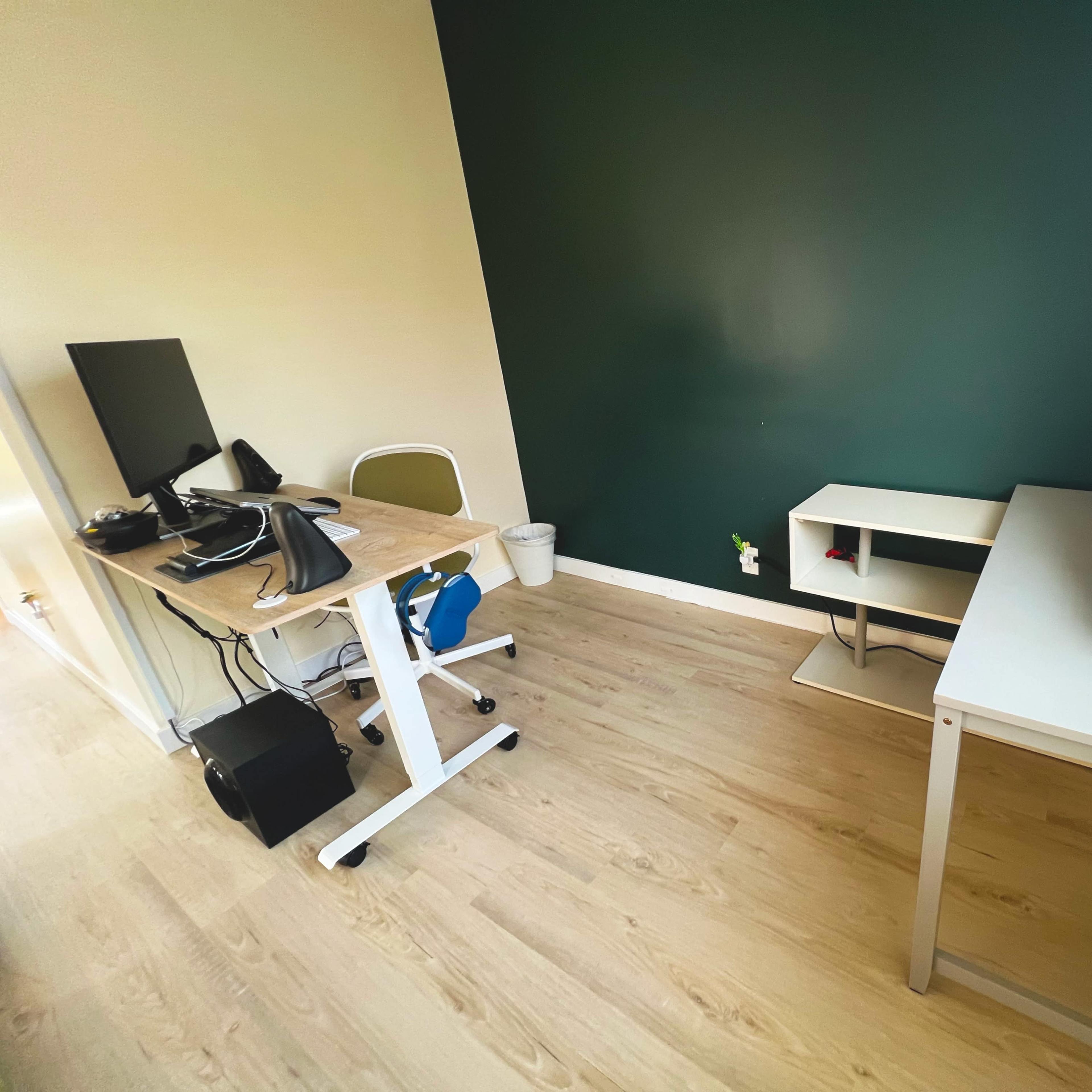 A small office space with a desktop computer setup on a desk, a white storage unit, and a green accent wall.
