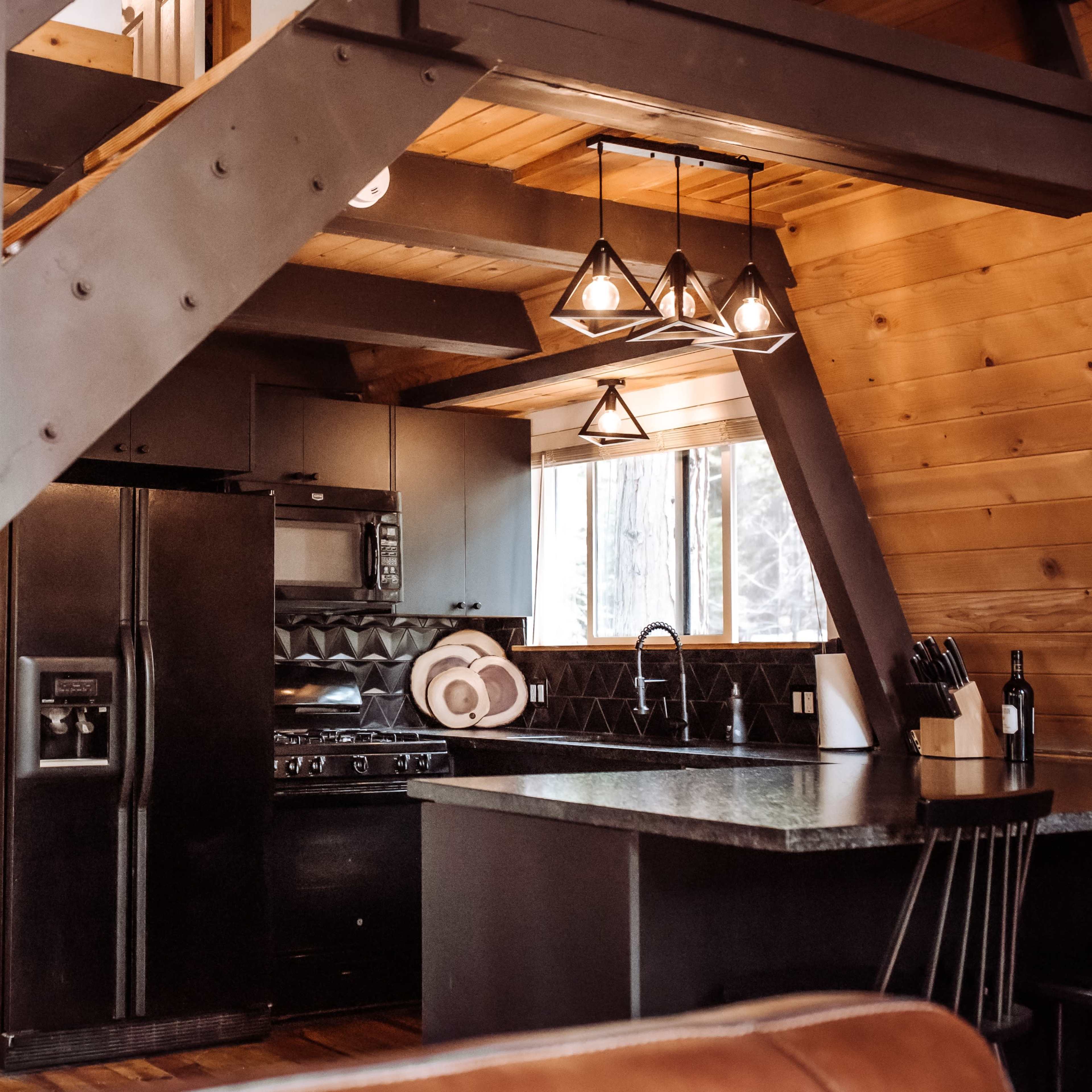 A modern kitchen with black appliances and a staircase featuring a metal frame and wooden steps.