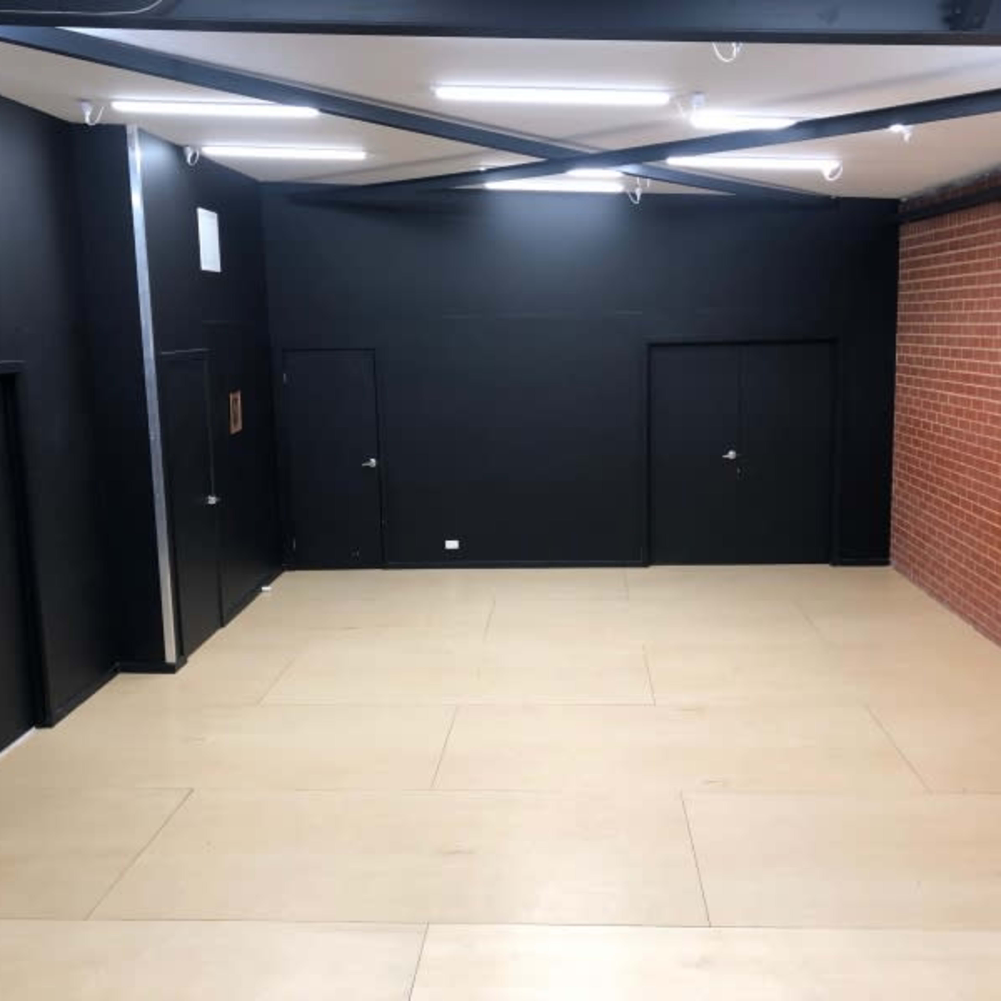 A spacious interior with black walls and two dark doors, alongside a section of exposed red brick wall, illuminated by overhead lights.