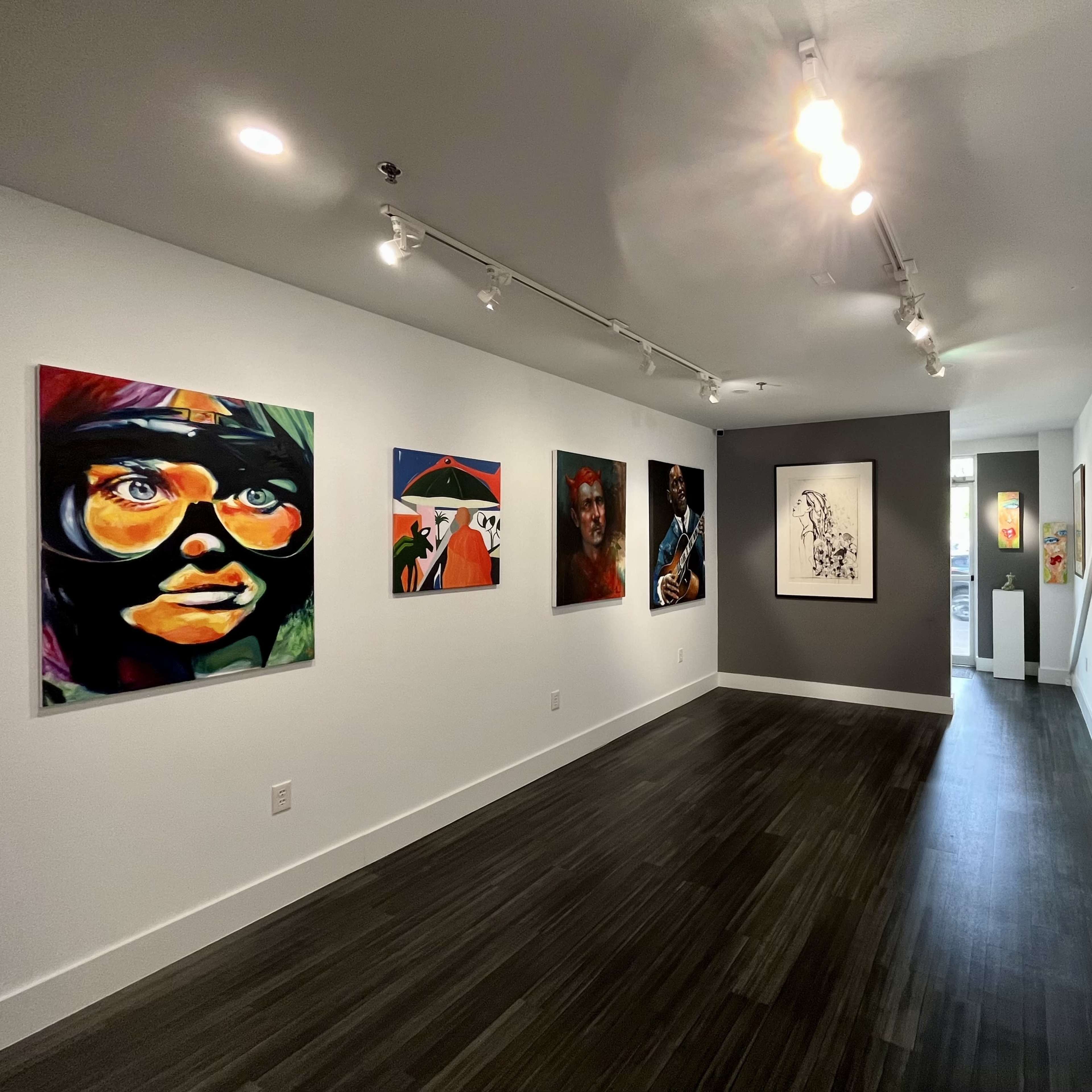 An art gallery interior featuring several colorful paintings on the walls with a corridor leading to another room at the end.