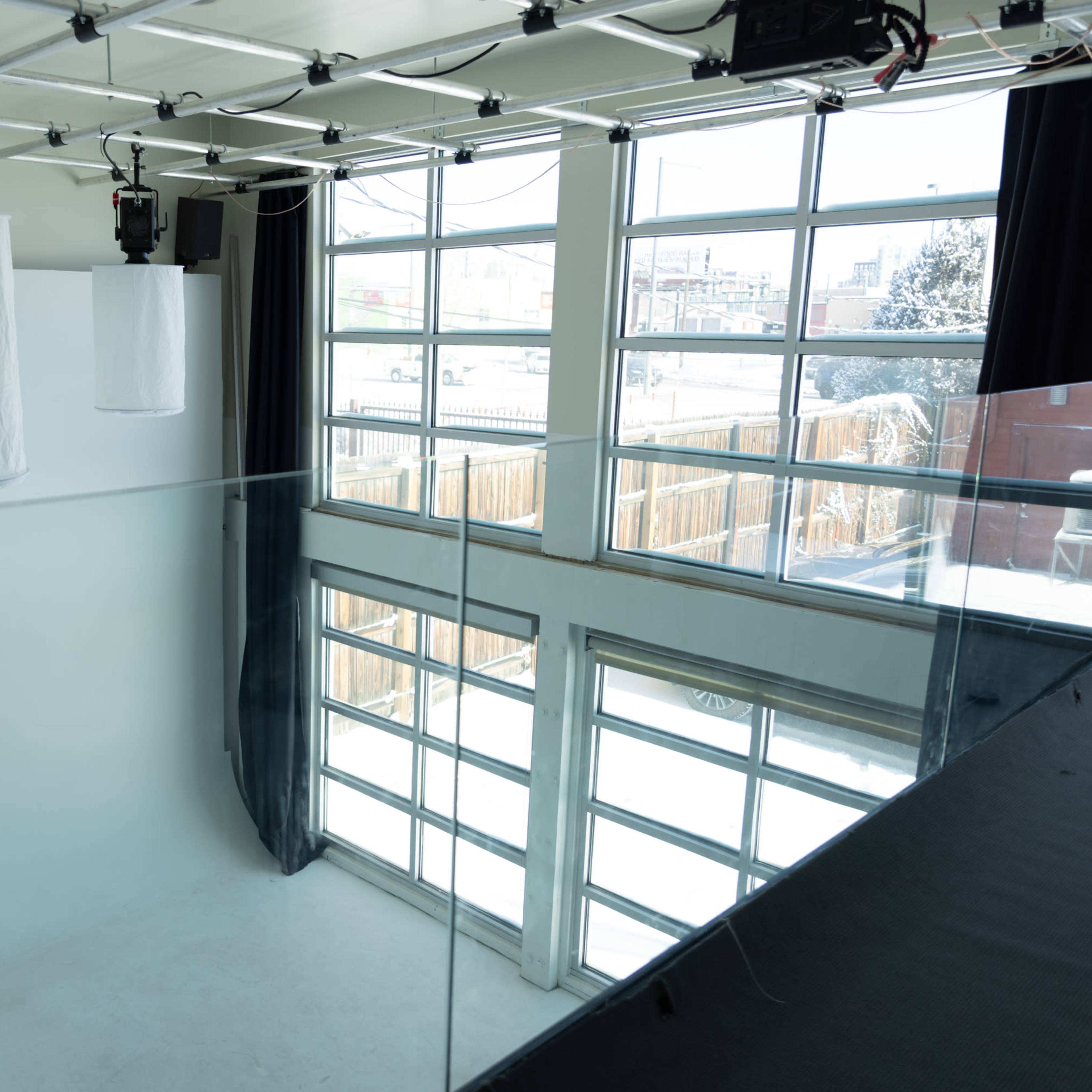A spacious photography studio with large windows, white backdrop, and overhead lighting fixtures.
