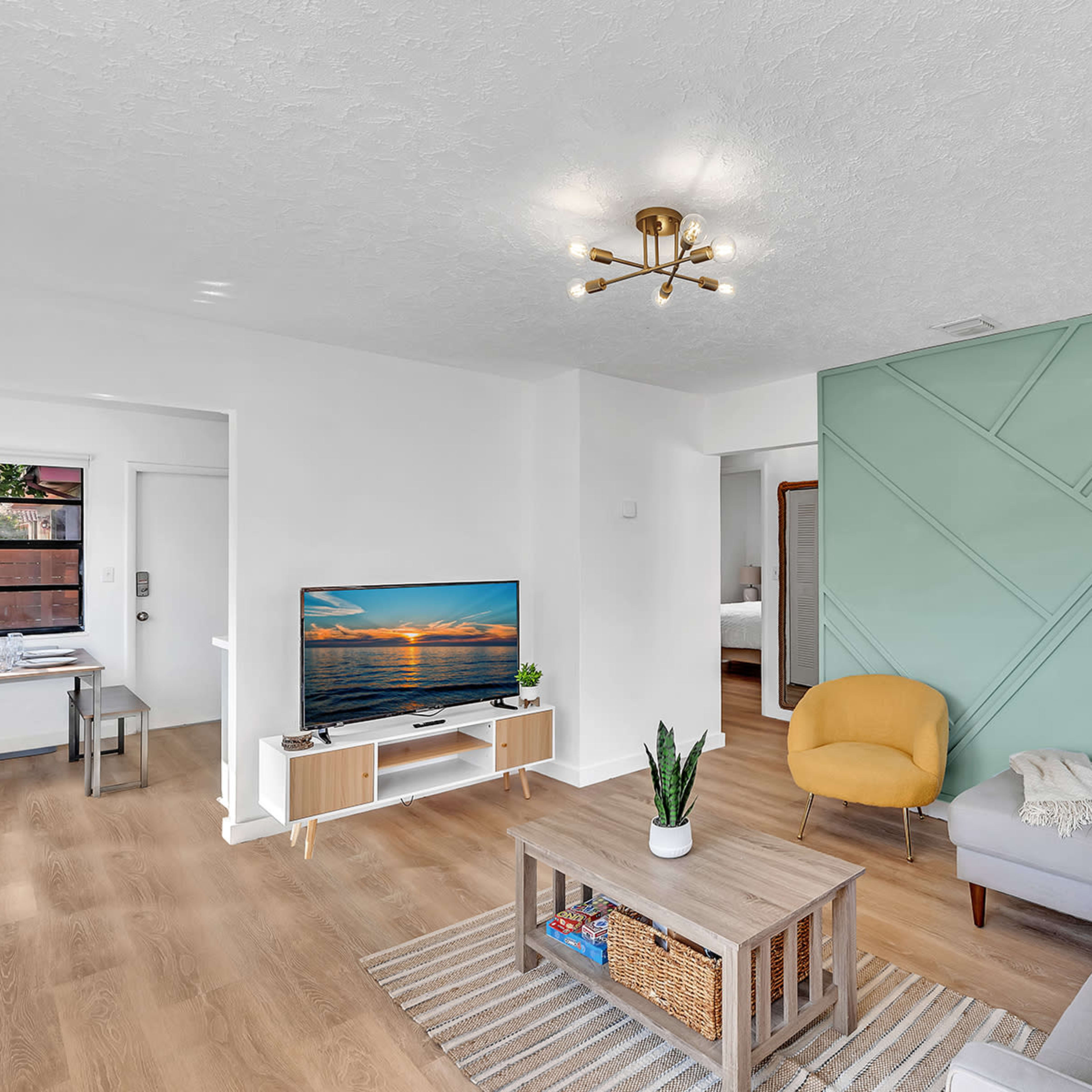 The living room features a gray sectional sofa, a wooden coffee table, and a television against a wall with a geometric green accent.
