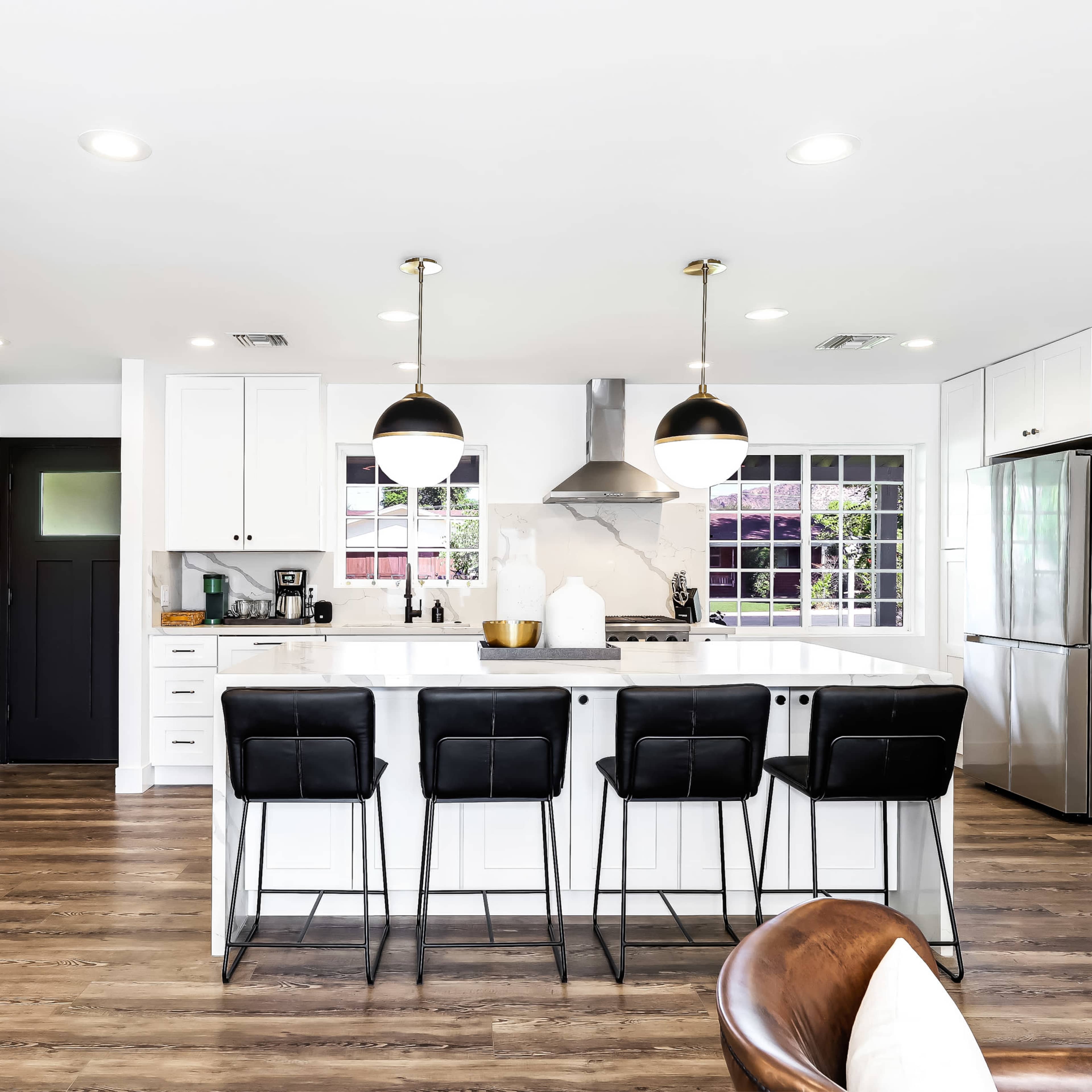 A modern kitchen features a large island with seating, black pendant lights, and stainless steel appliances.