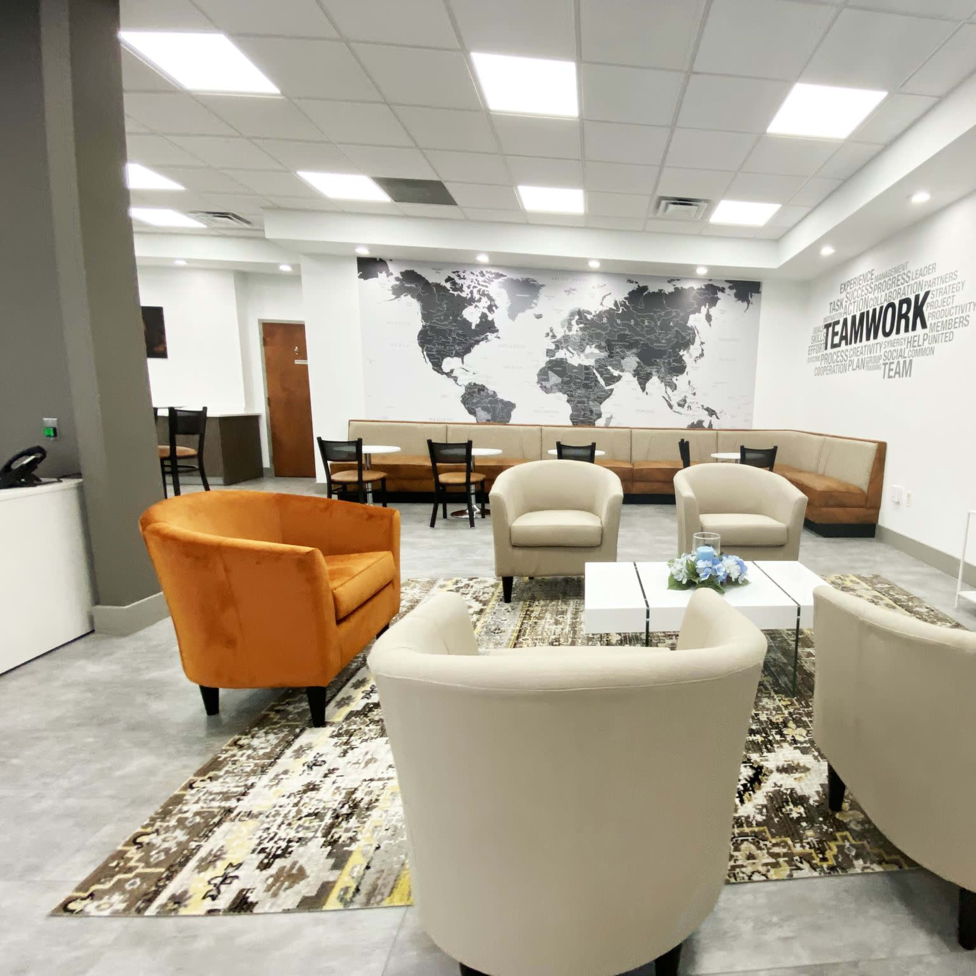 A modern lounge area featuring orange and beige armchairs, a large map on the wall, and several tables and chairs arranged for seating.