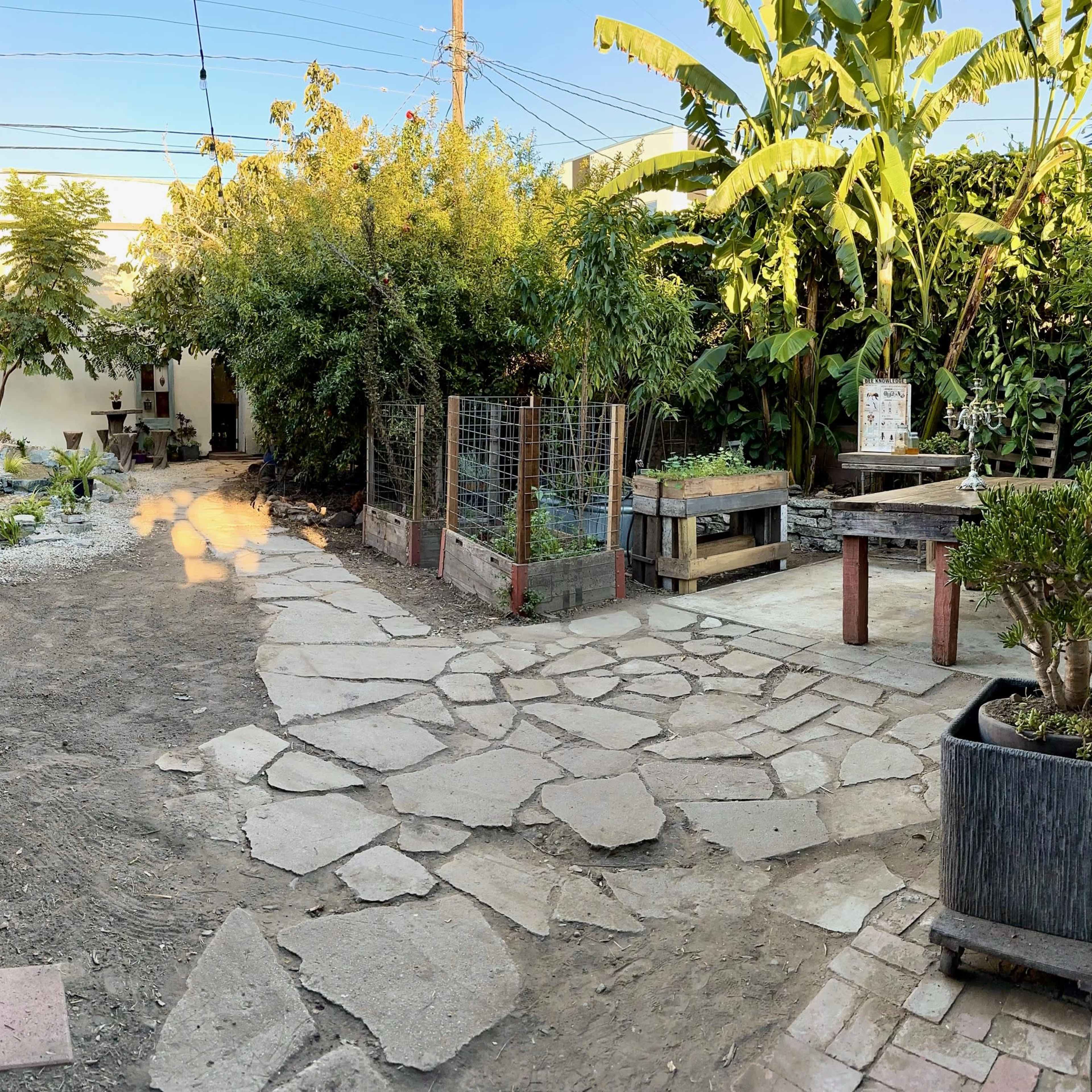 A landscaped garden path made of stone, bordered by various plants, trees, and garden beds.