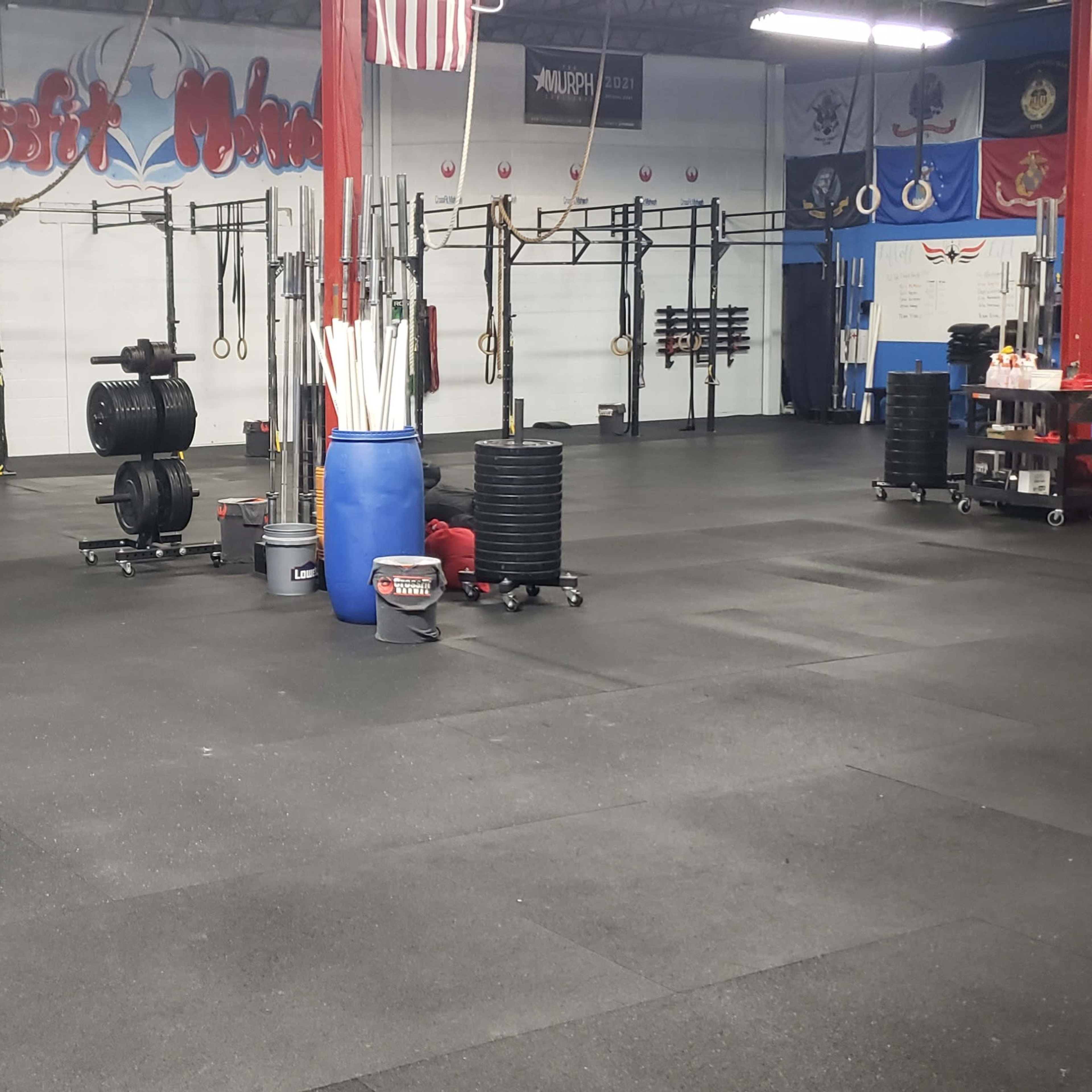 The interior of a gym with workout equipment, including weights and squat racks, arranged in an organized space with rubber flooring.