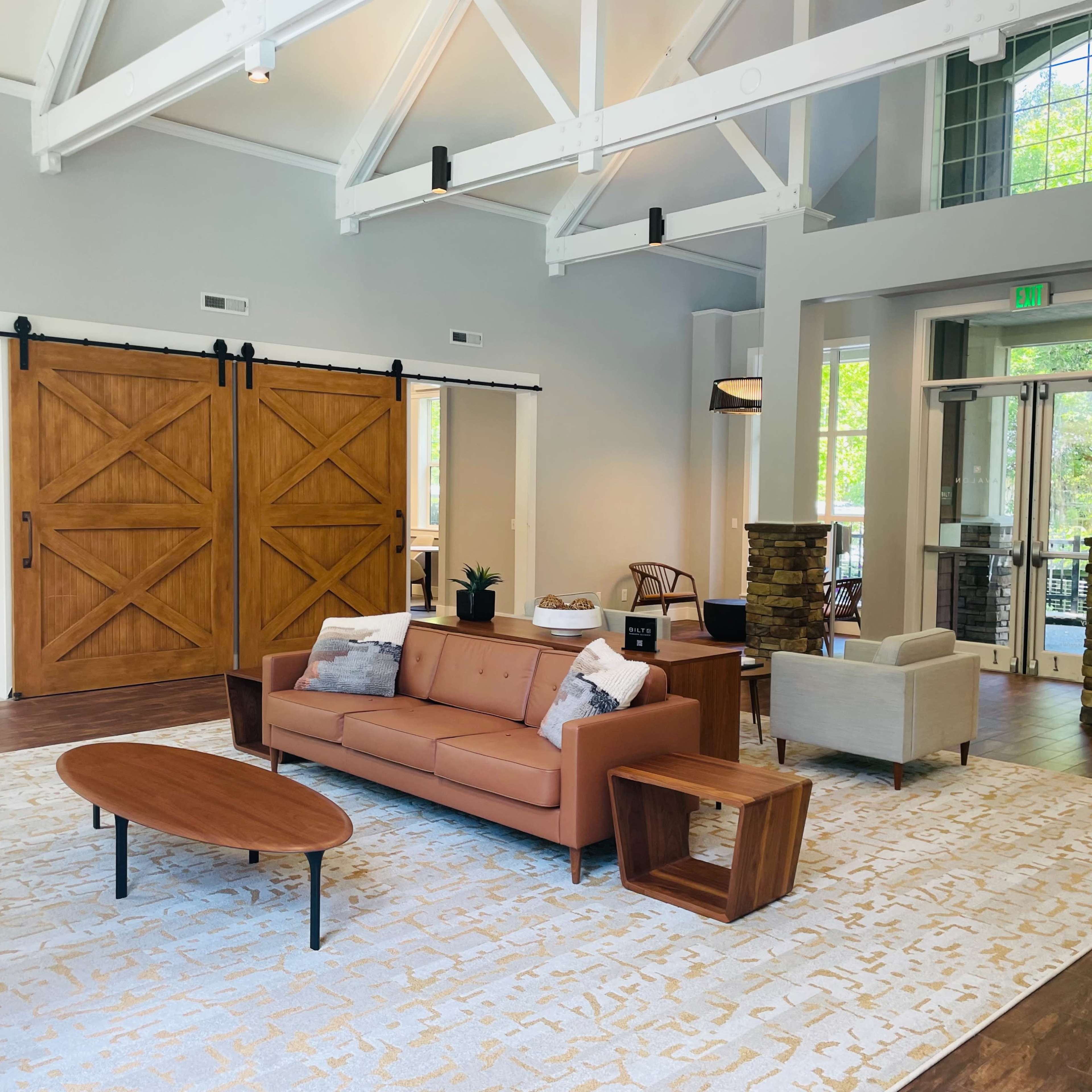 A spacious, modern lobby area featuring a brown sofa, a coffee table, and large sliding wooden doors.