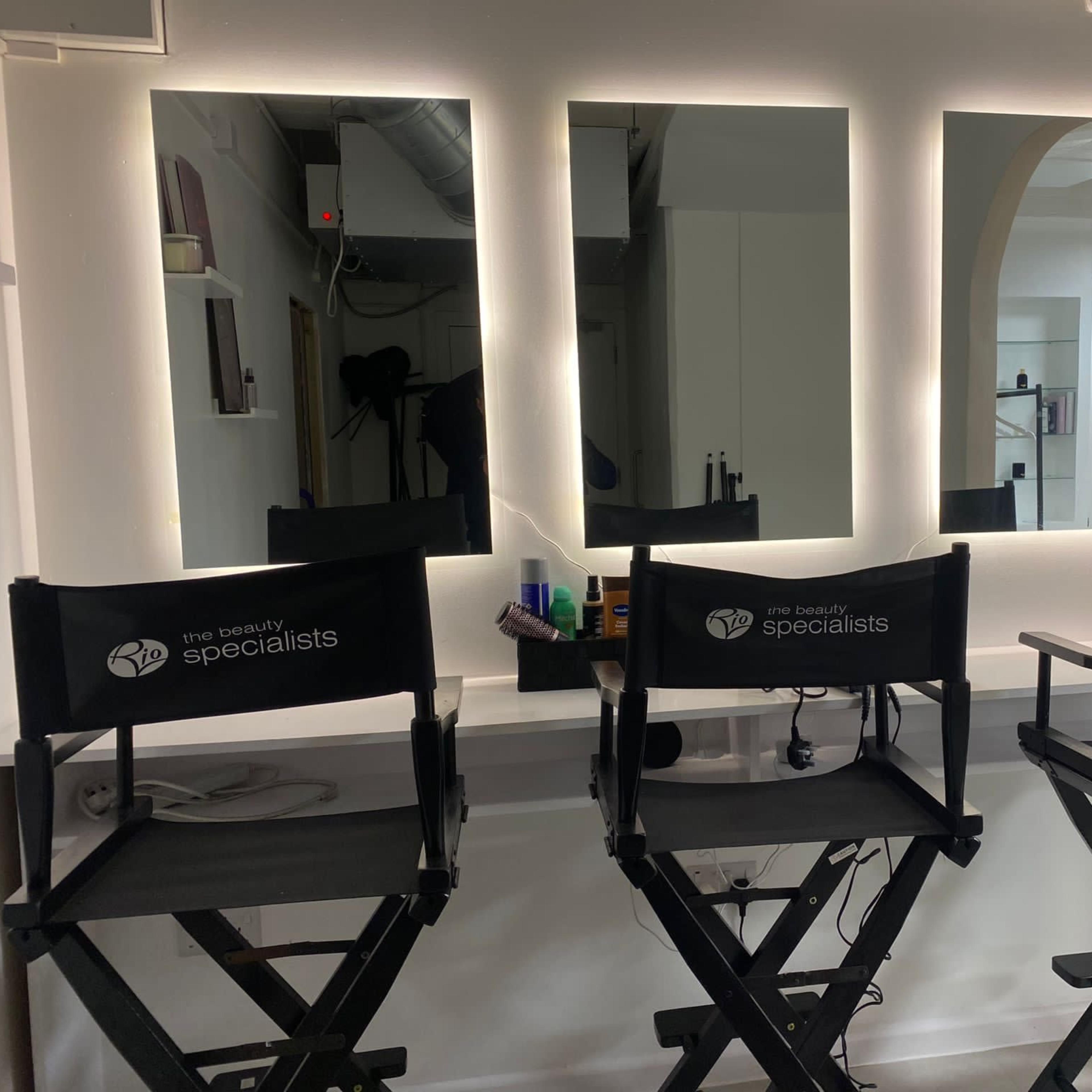 Three director's chairs are positioned in front of three illuminated mirrors in a beauty salon.