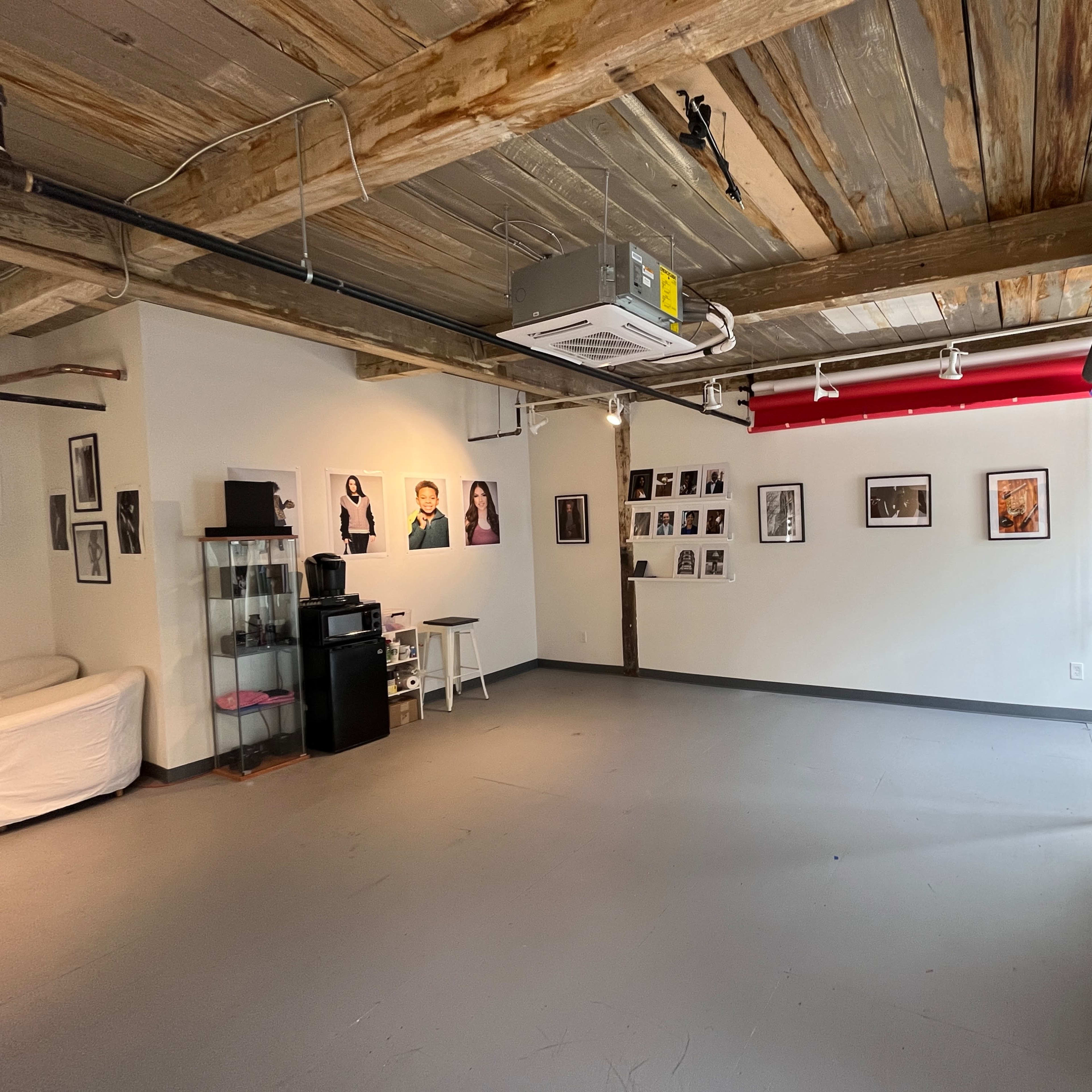 A spacious room with exposed wooden beams, featuring various framed photographs on the walls, a couch, and storage shelves on one side.
