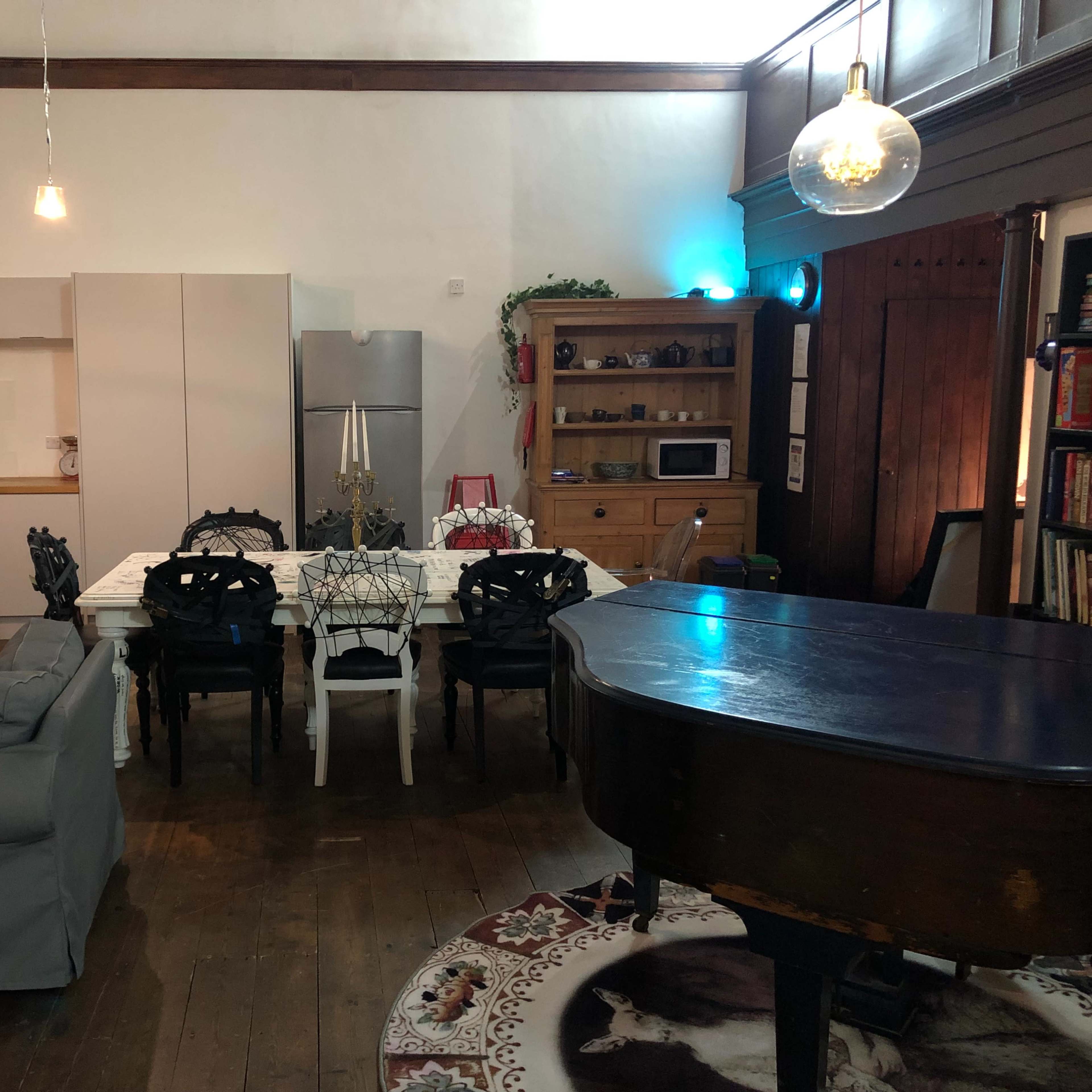 A spacious interior with a dining table surrounded by chairs, a grand piano, and a combination of modern and wooden furniture.