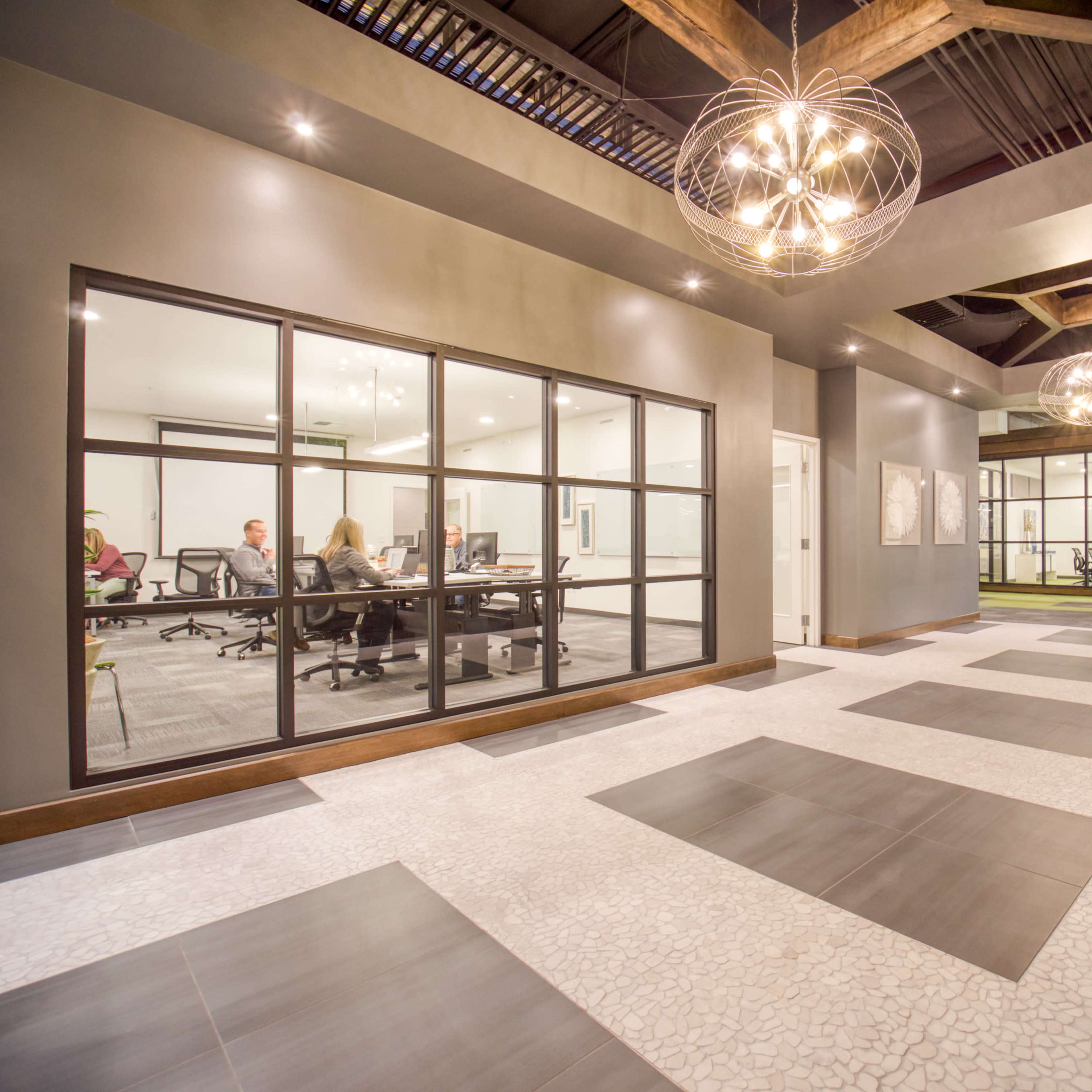 A modern office space featuring a large, open area with a glass-walled meeting room and decorative lighting overhead.