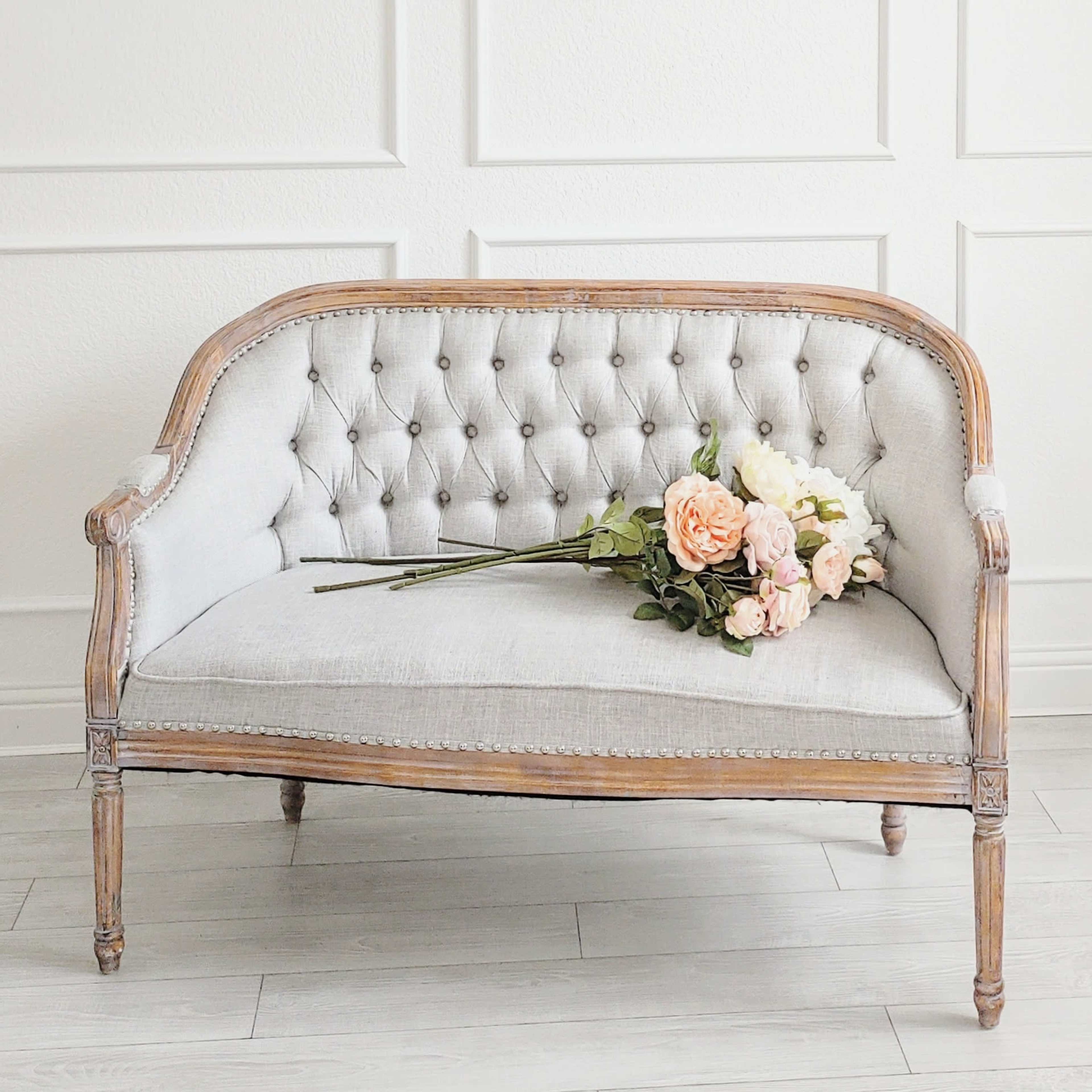 A vintage tufted sofa with a wooden frame sits against a wall, adorned with a bouquet of flowers resting on the seat.