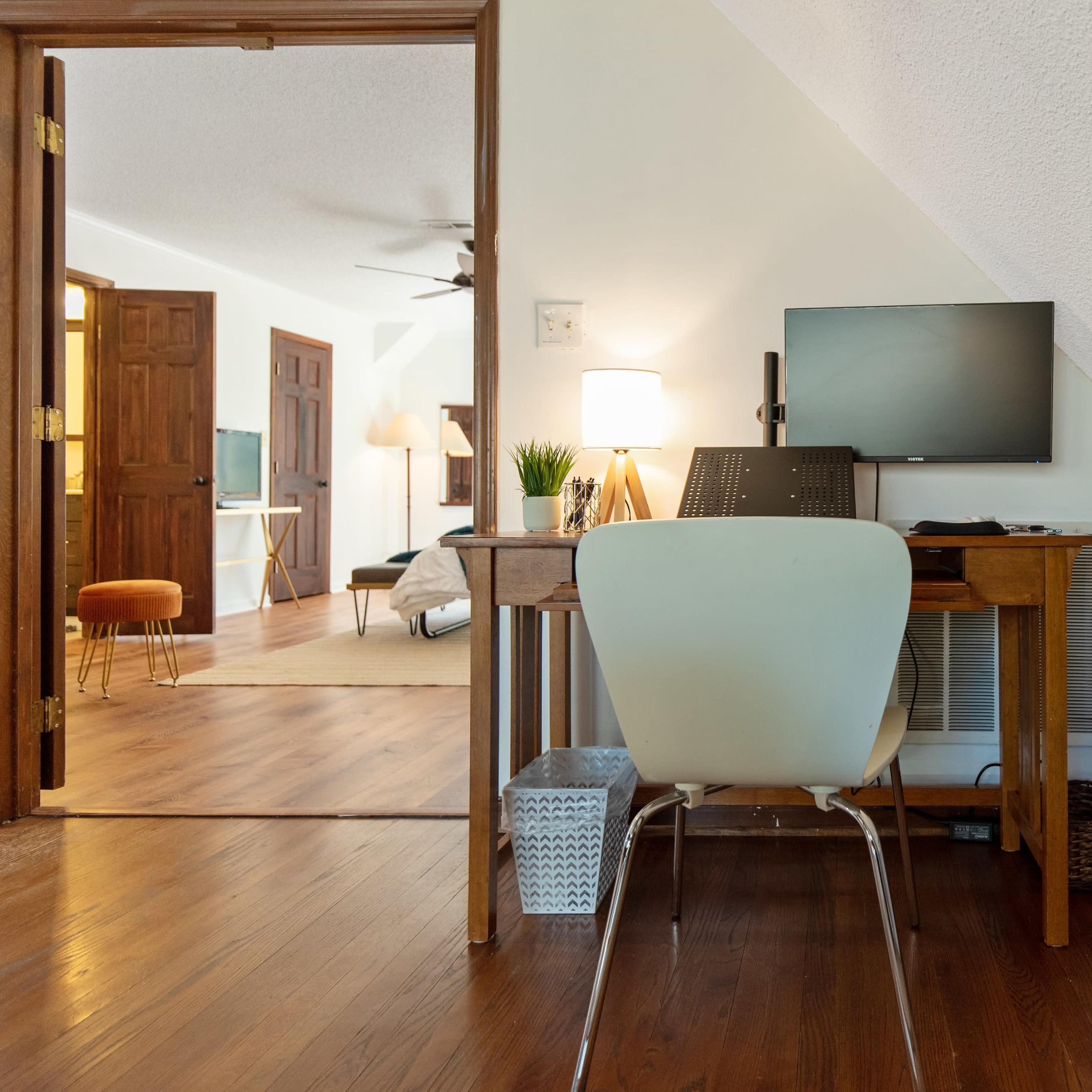 A small home office features a wooden desk with a computer and a chair, adjacent to a brightly decorated wall and an open doorway leading to another room.