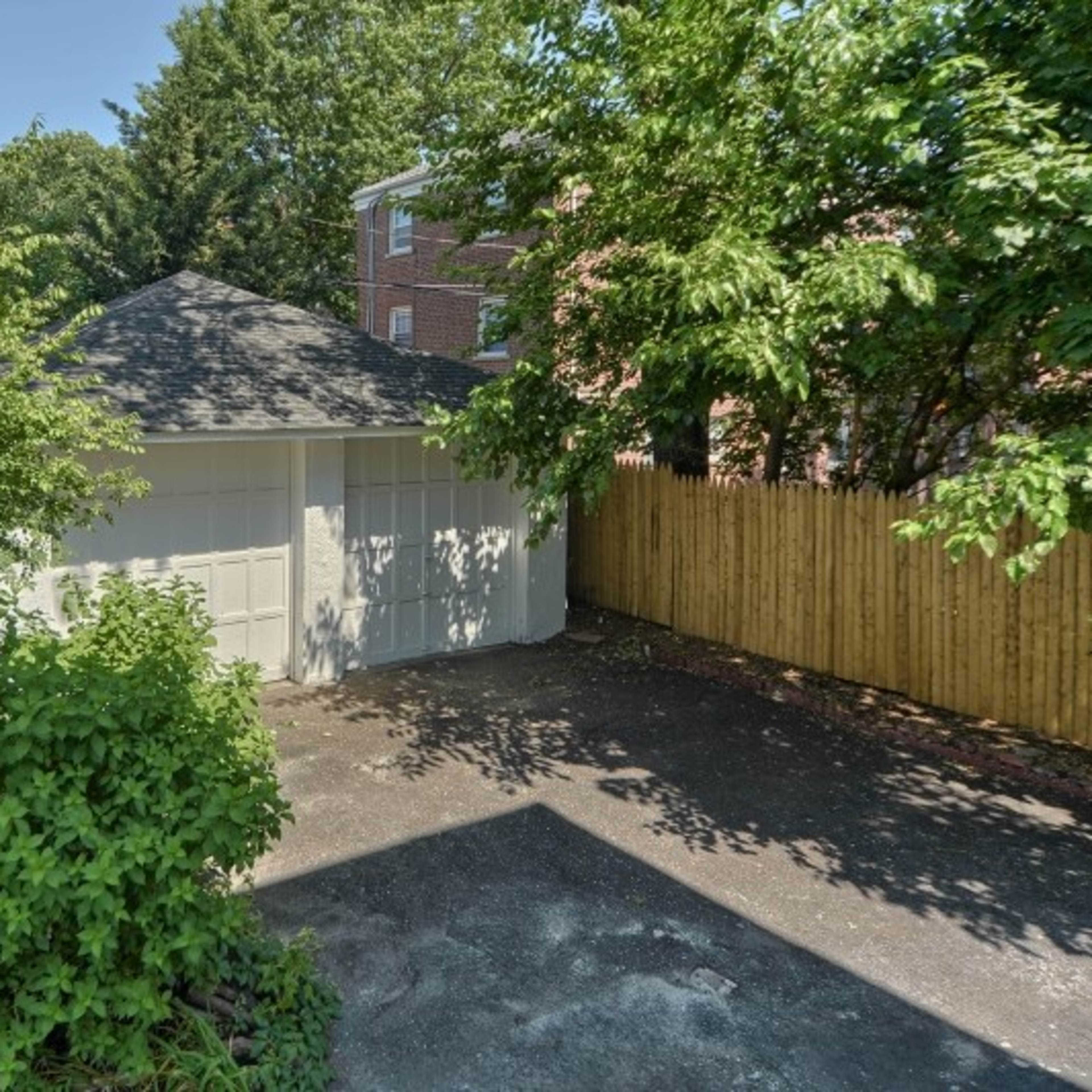 A detached garage surrounded by trees and a wooden fence in a residential area.