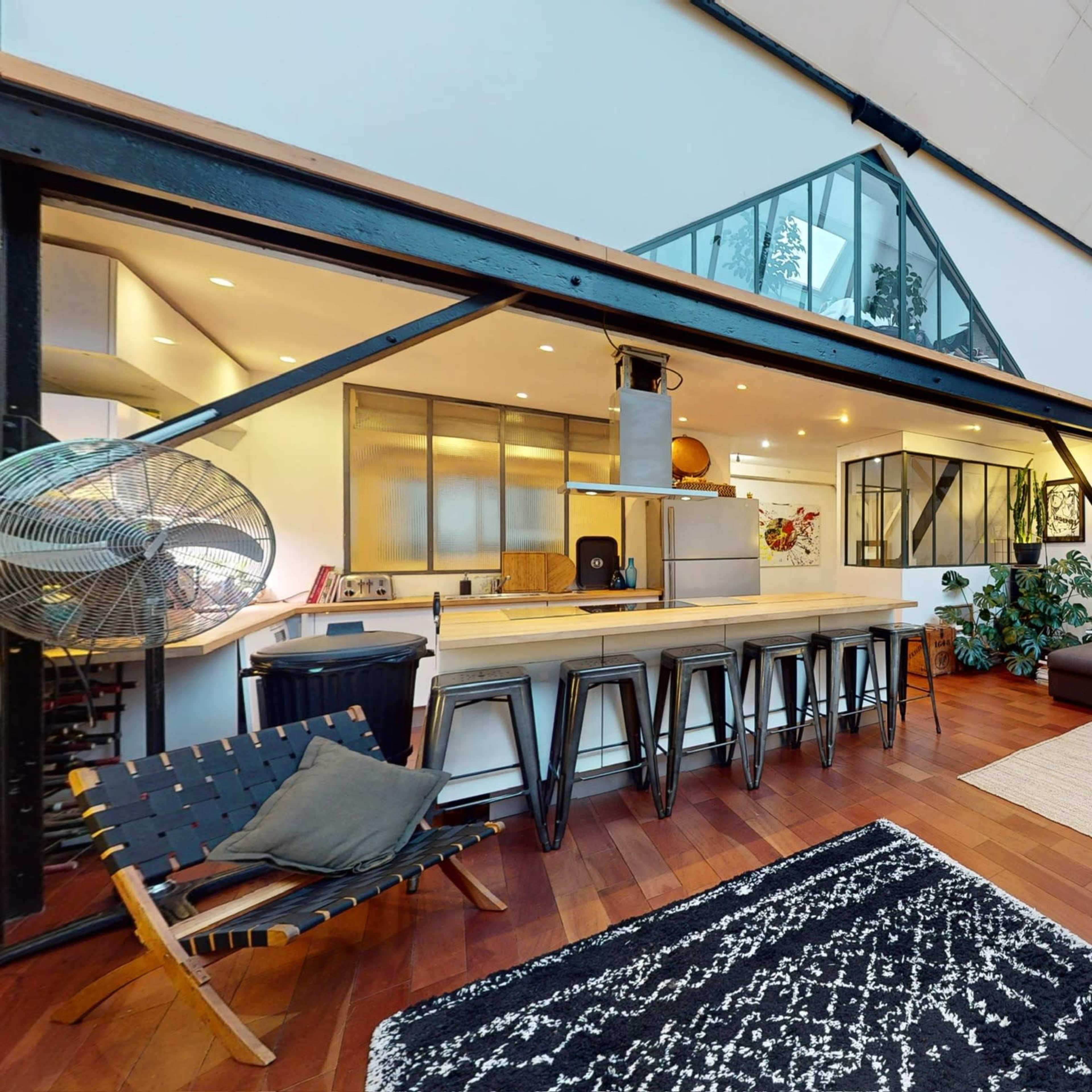 A spacious, modern living area with a kitchen, dining space, and a lounge featuring large windows and wooden flooring.