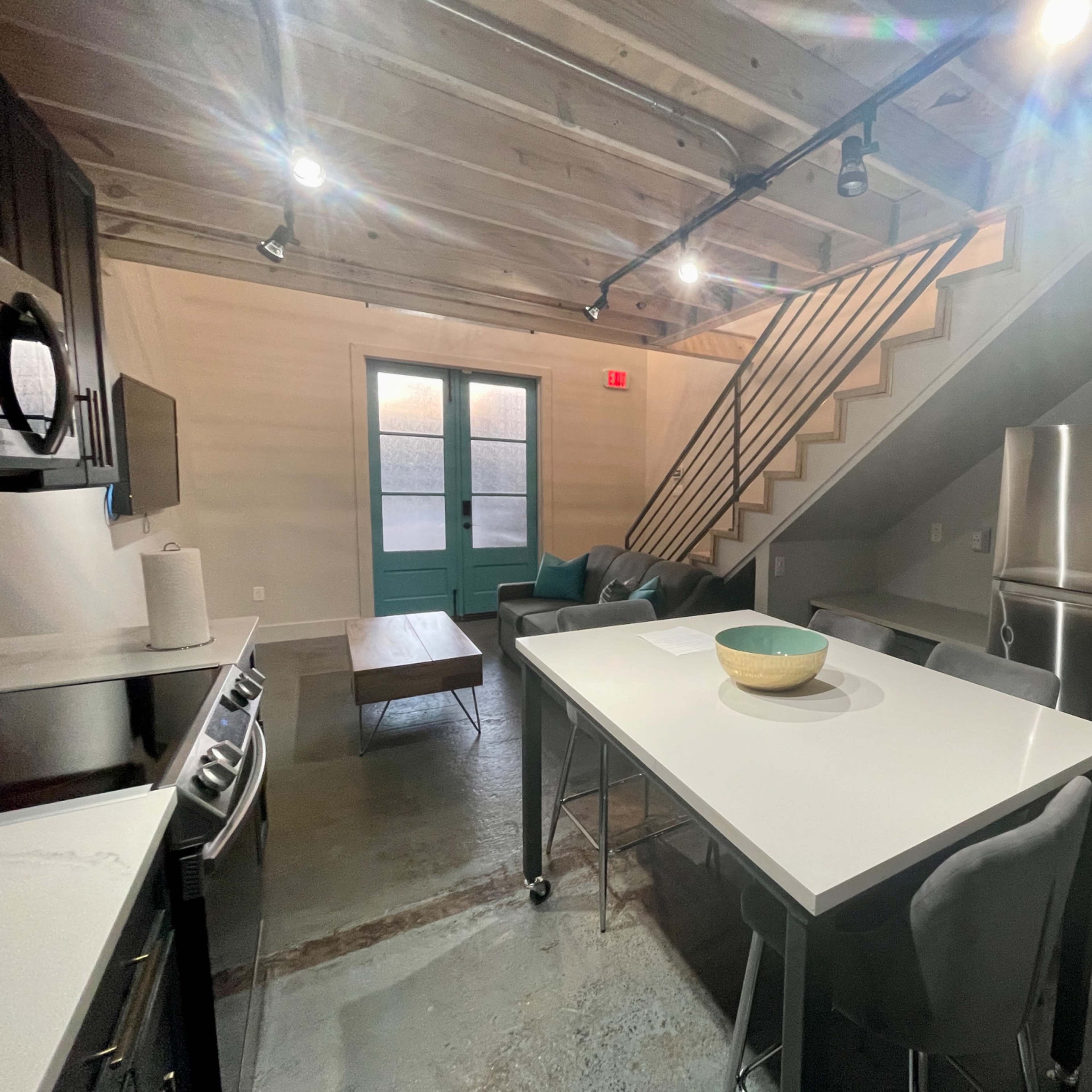 A modern kitchen with gray cabinetry, a large island with a bowl on it, and a staircase leading to an upper level.