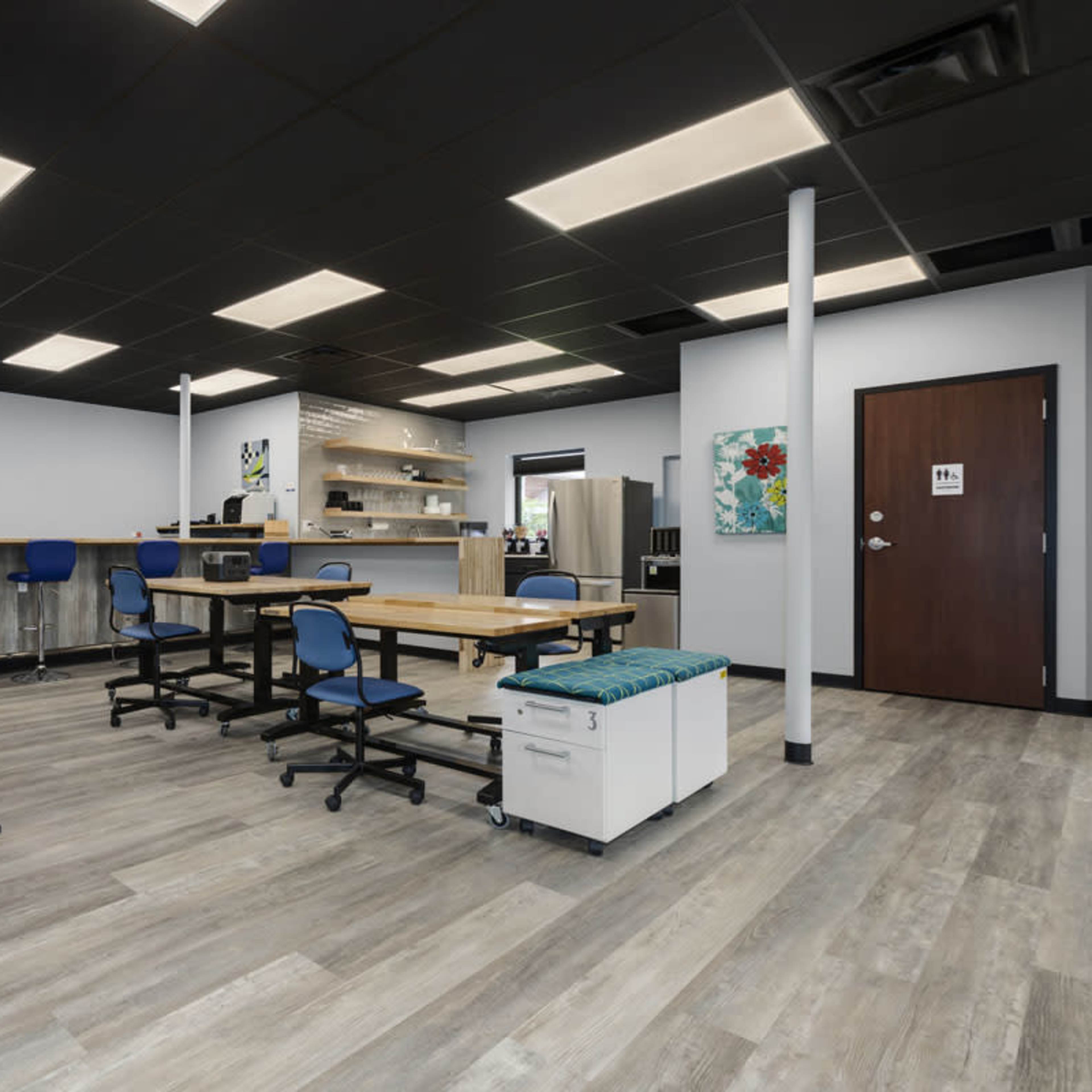 A modern office space featuring a kitchenette, tables with chairs, and a ramp for accessibility.