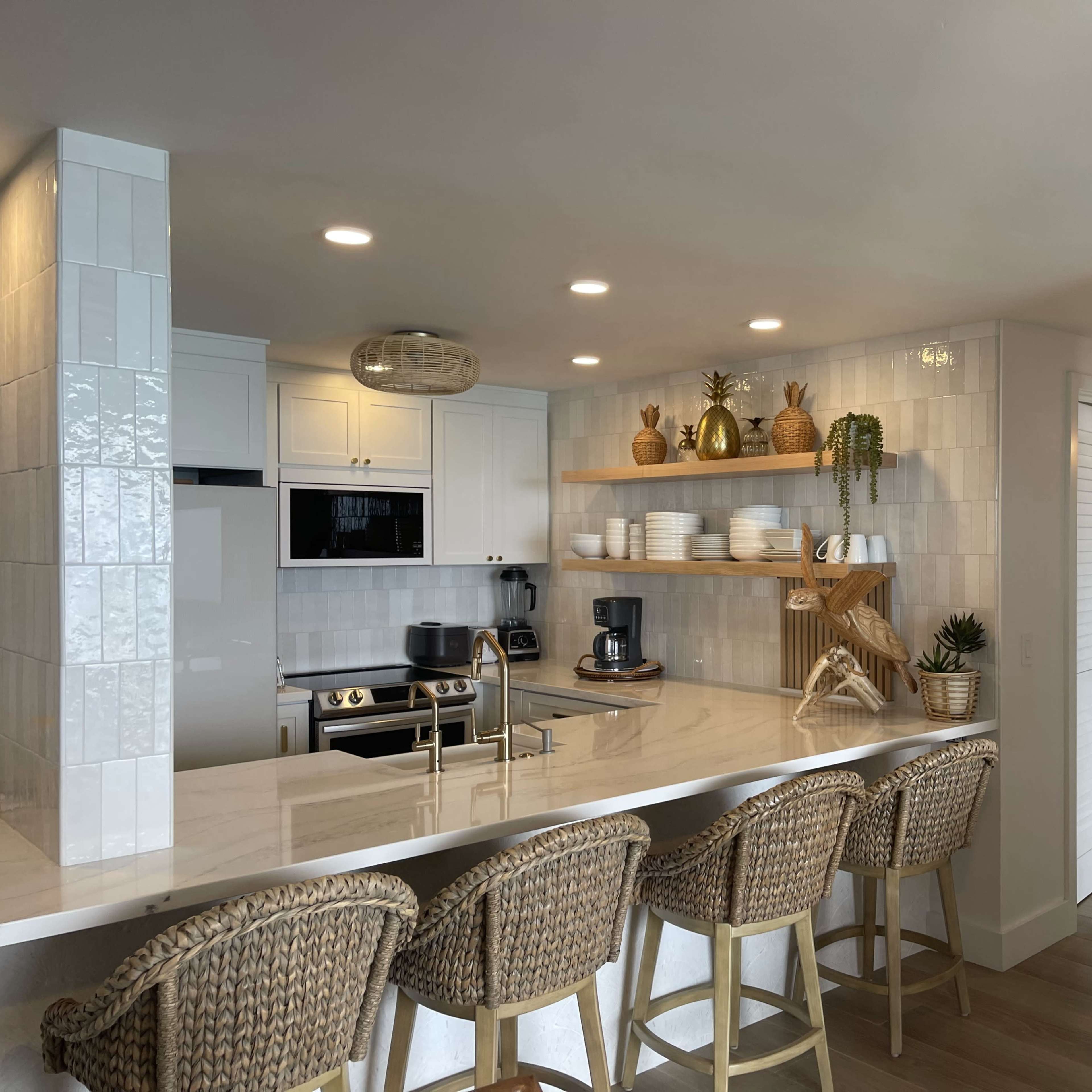 A modern kitchen with white cabinets, a marble countertop, and bar stools, featuring open shelving that displays dishware and decorative plants.