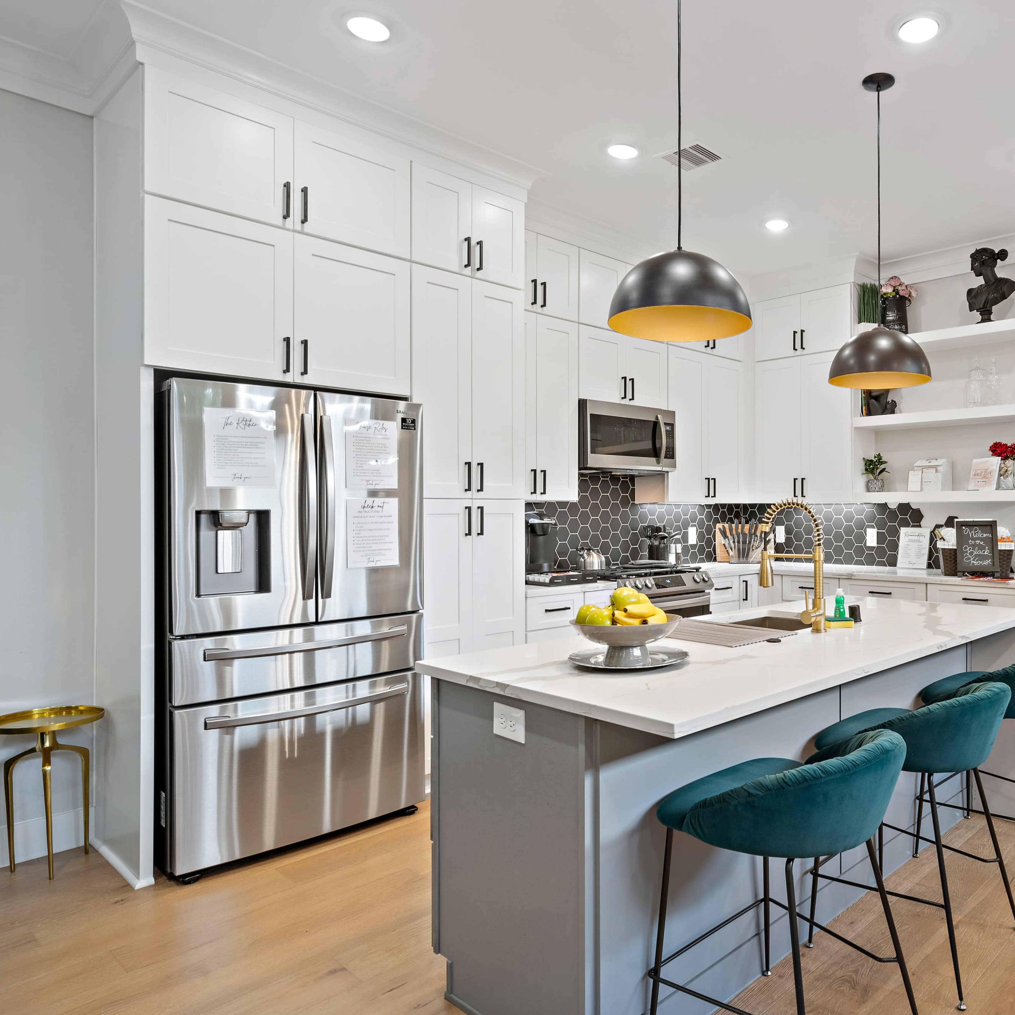 A modern kitchen features white cabinetry, stainless steel appliances, a large island with seating, and decorative pendant lighting.