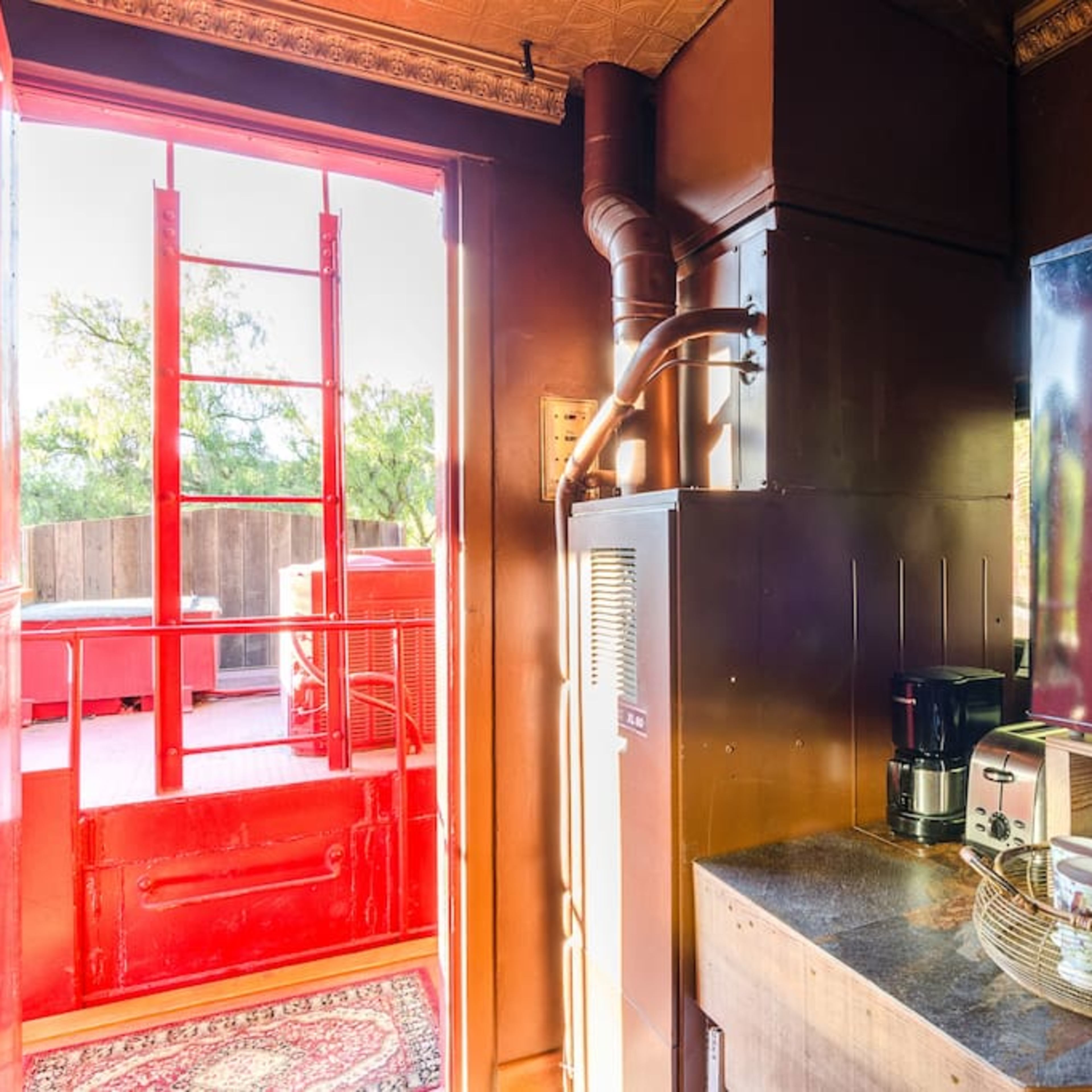 A kitchenette area with a large black TV, coffee maker, and a doorway leading to an outdoor space featuring a red railing.