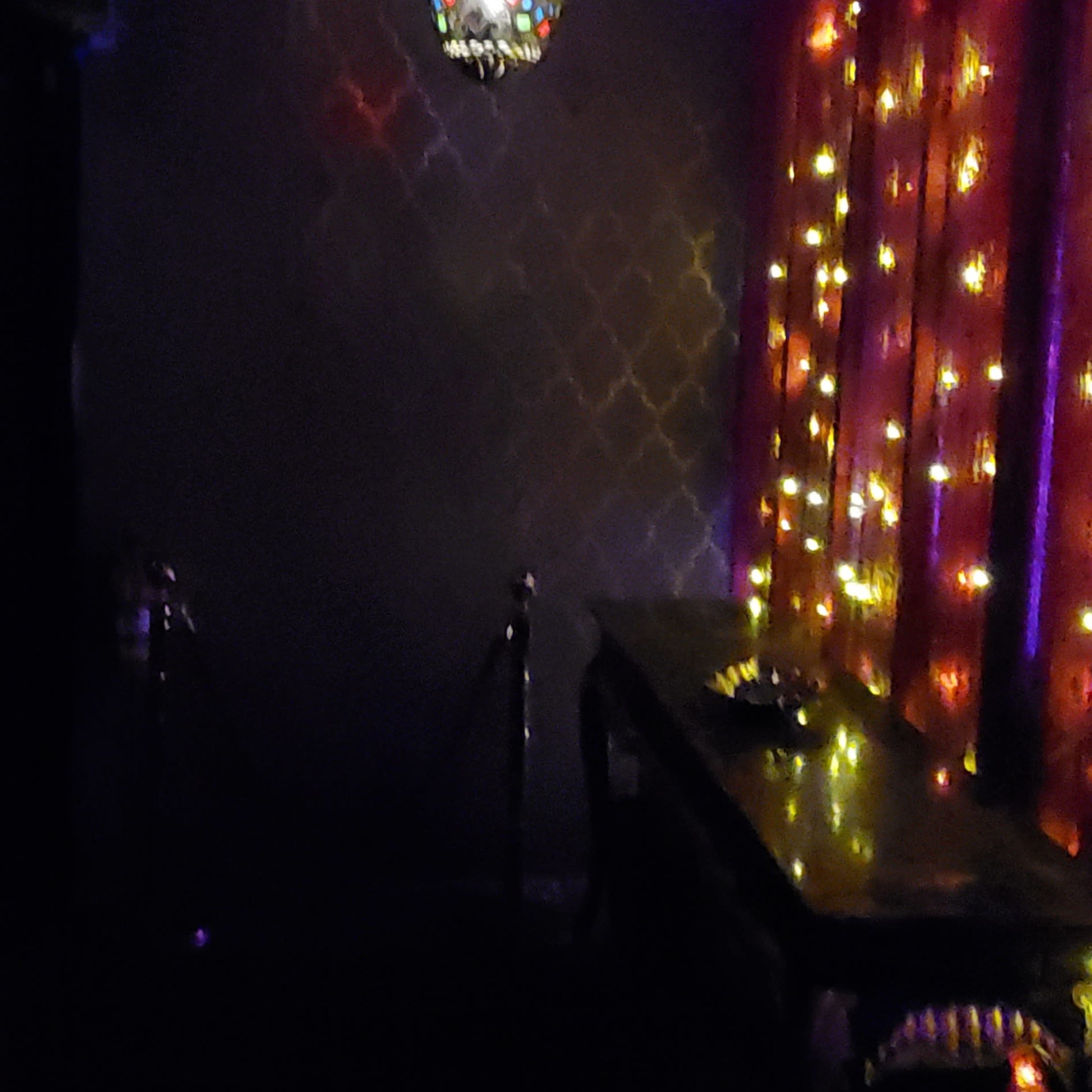 A dimly lit room with a colorful chandelier hanging from the ceiling and walls adorned with illuminated patterns.
