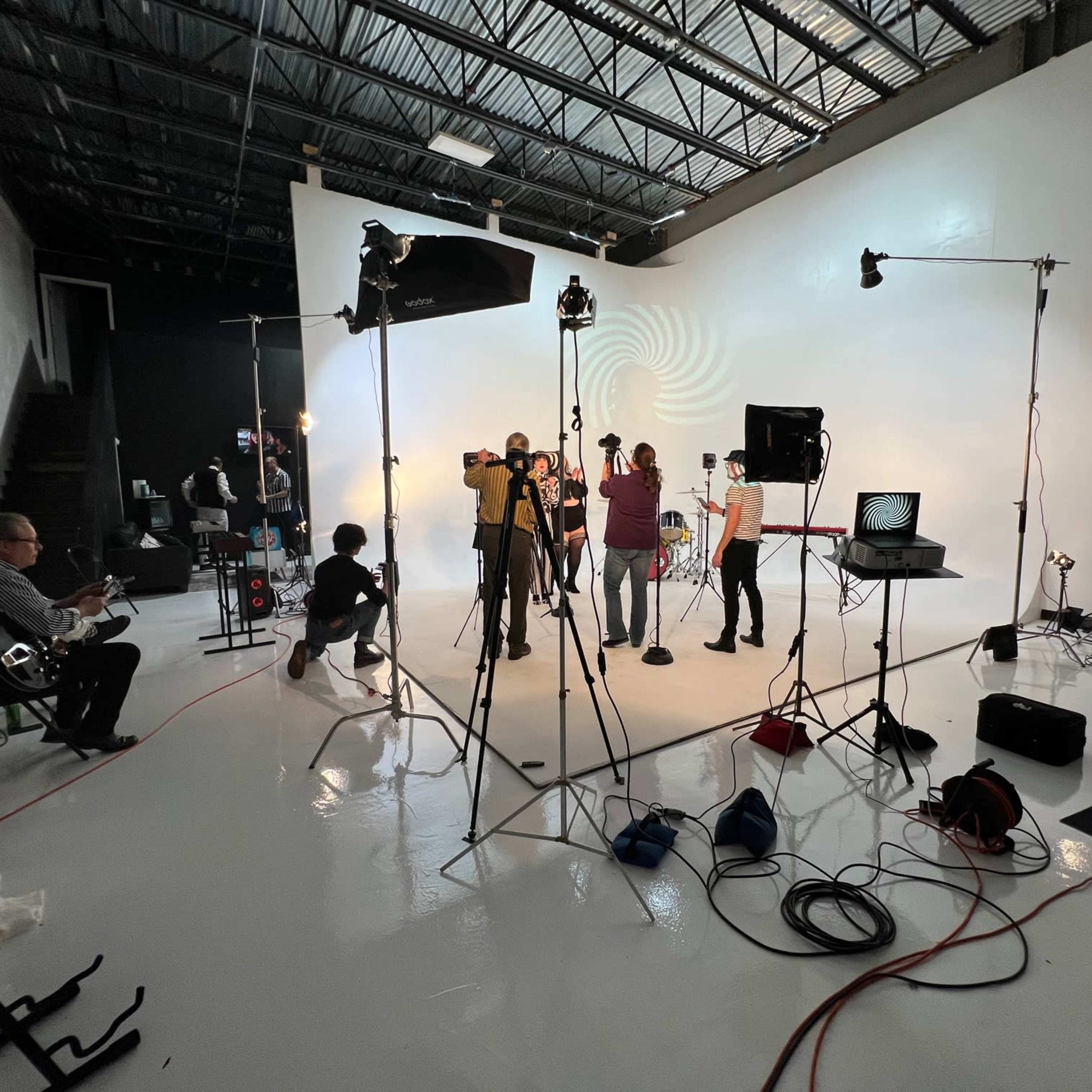 A photo studio is set up with a crew filming a music video, surrounded by various lighting and audio equipment.
