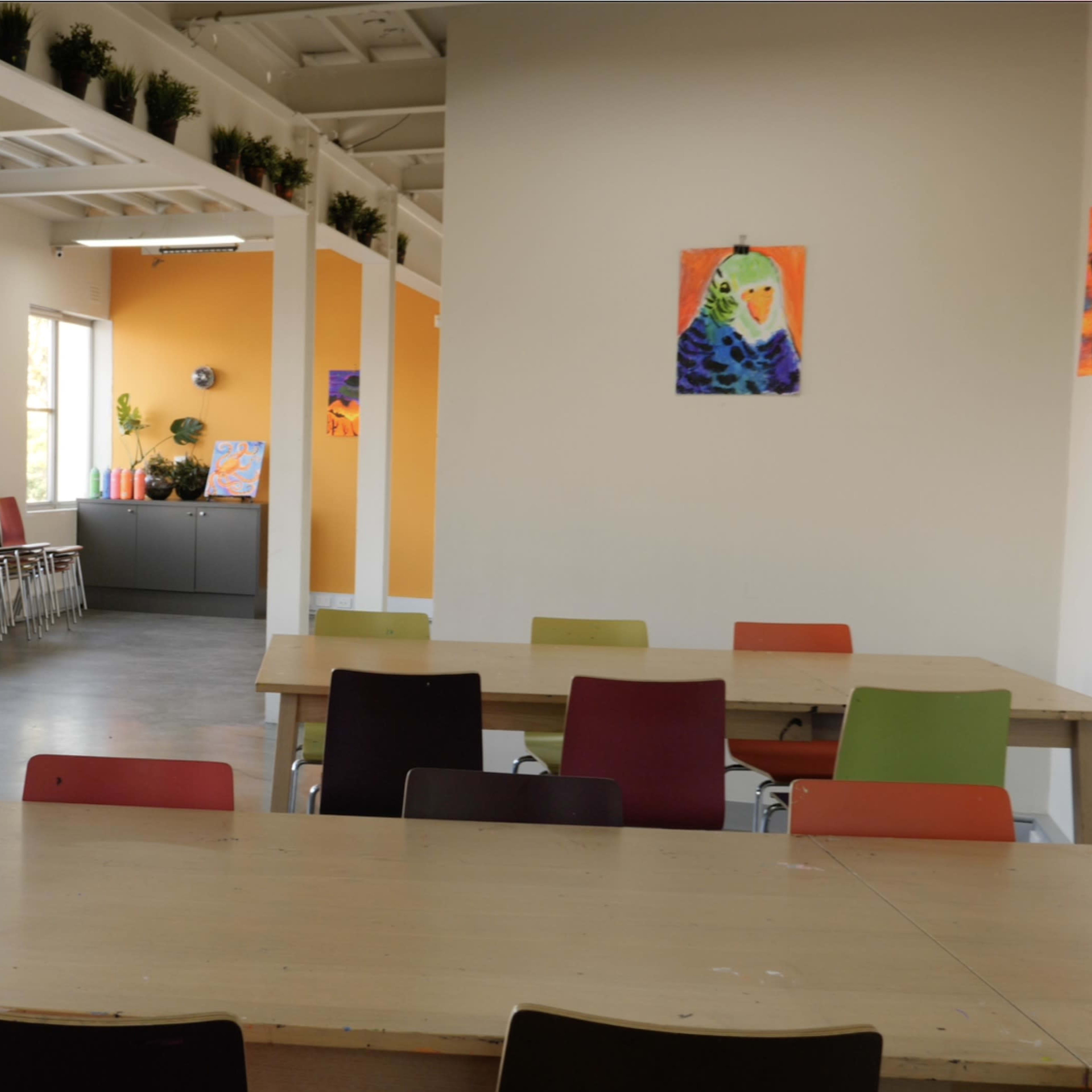 A modern classroom with tables and chairs arranged along with colorful artwork displayed on the walls.