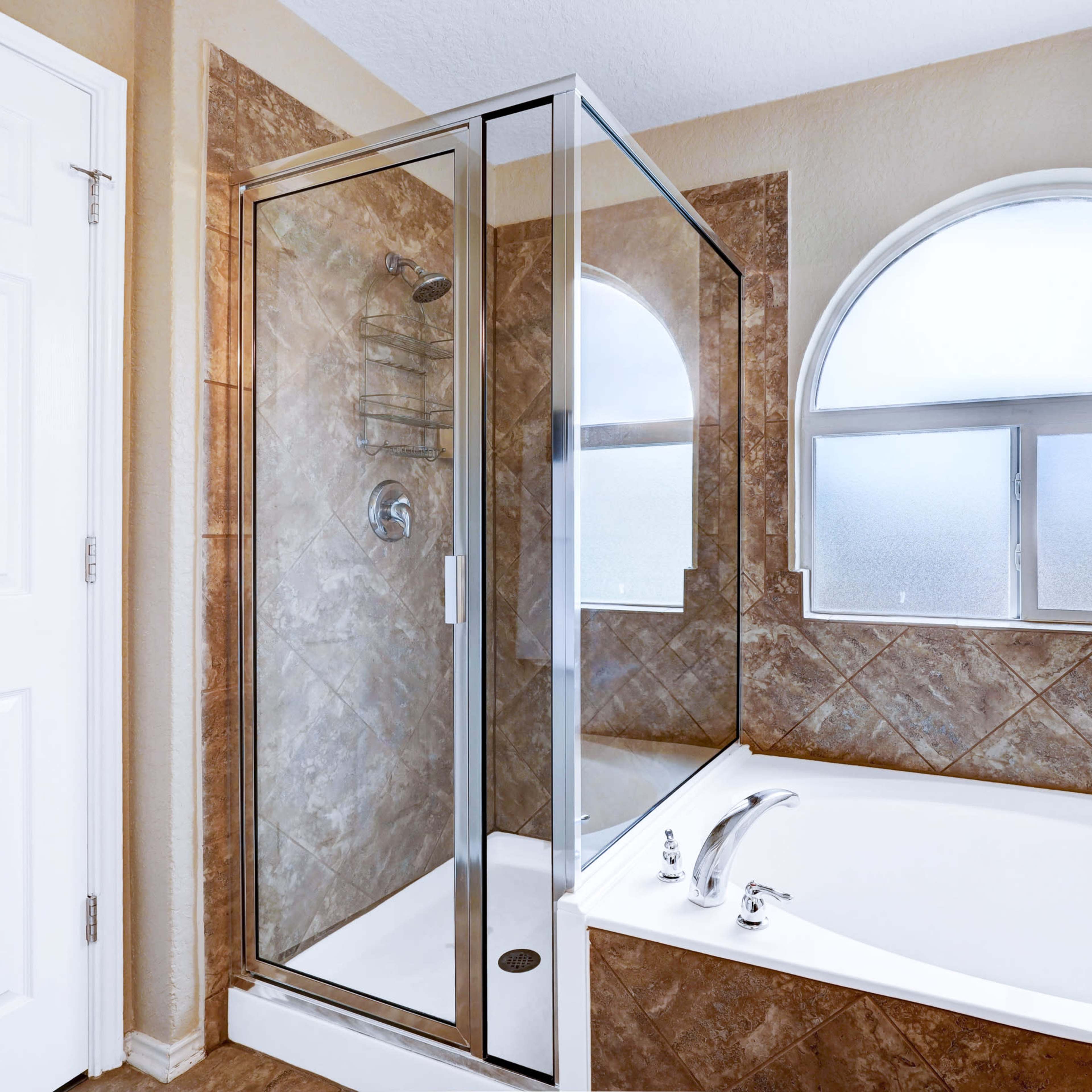A bathroom featuring a glass shower enclosure next to a freestanding bathtub, with an arched window allowing light in.