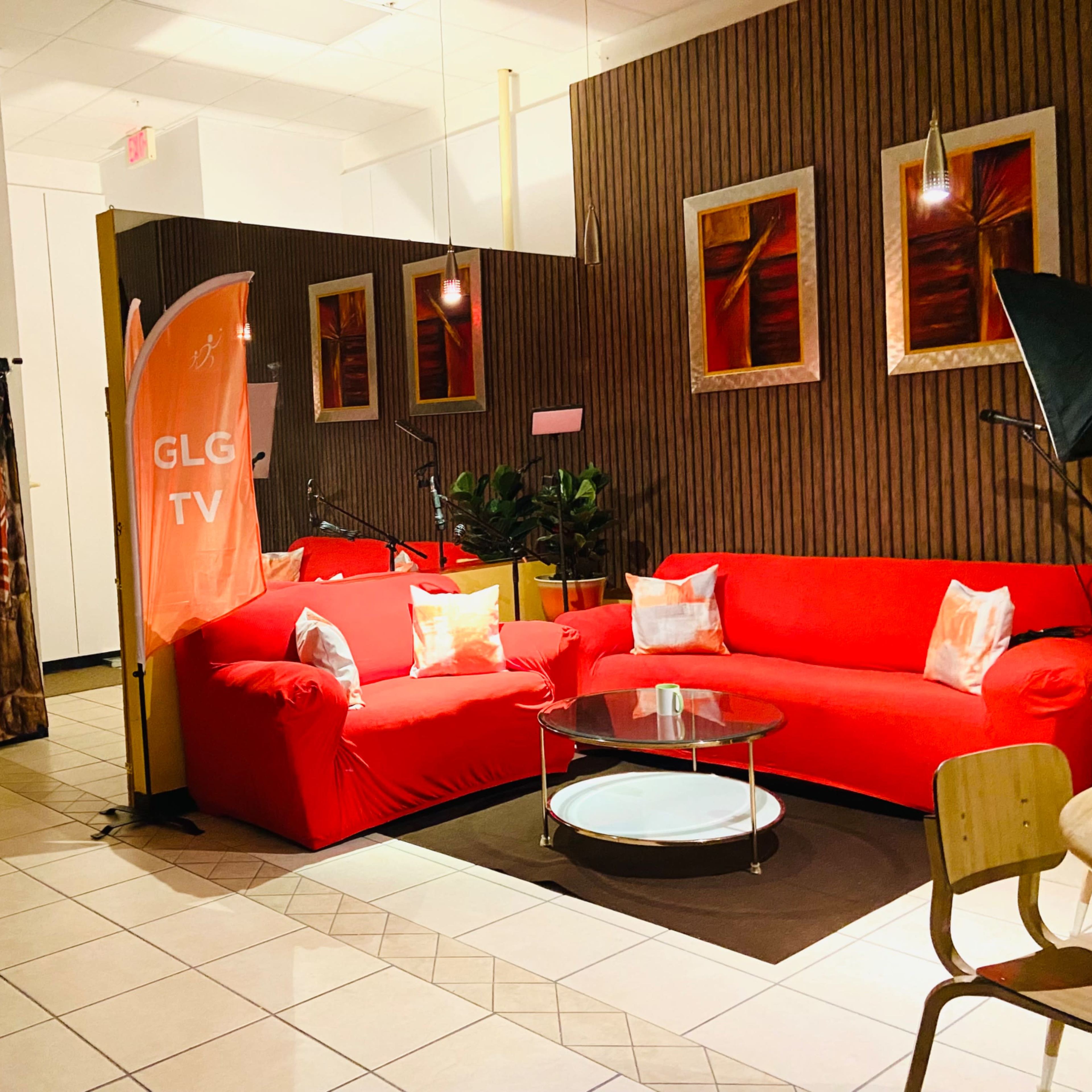 A seating area with red couches, a glass coffee table, a decorative fireplace backdrop, and framed art on the walls.