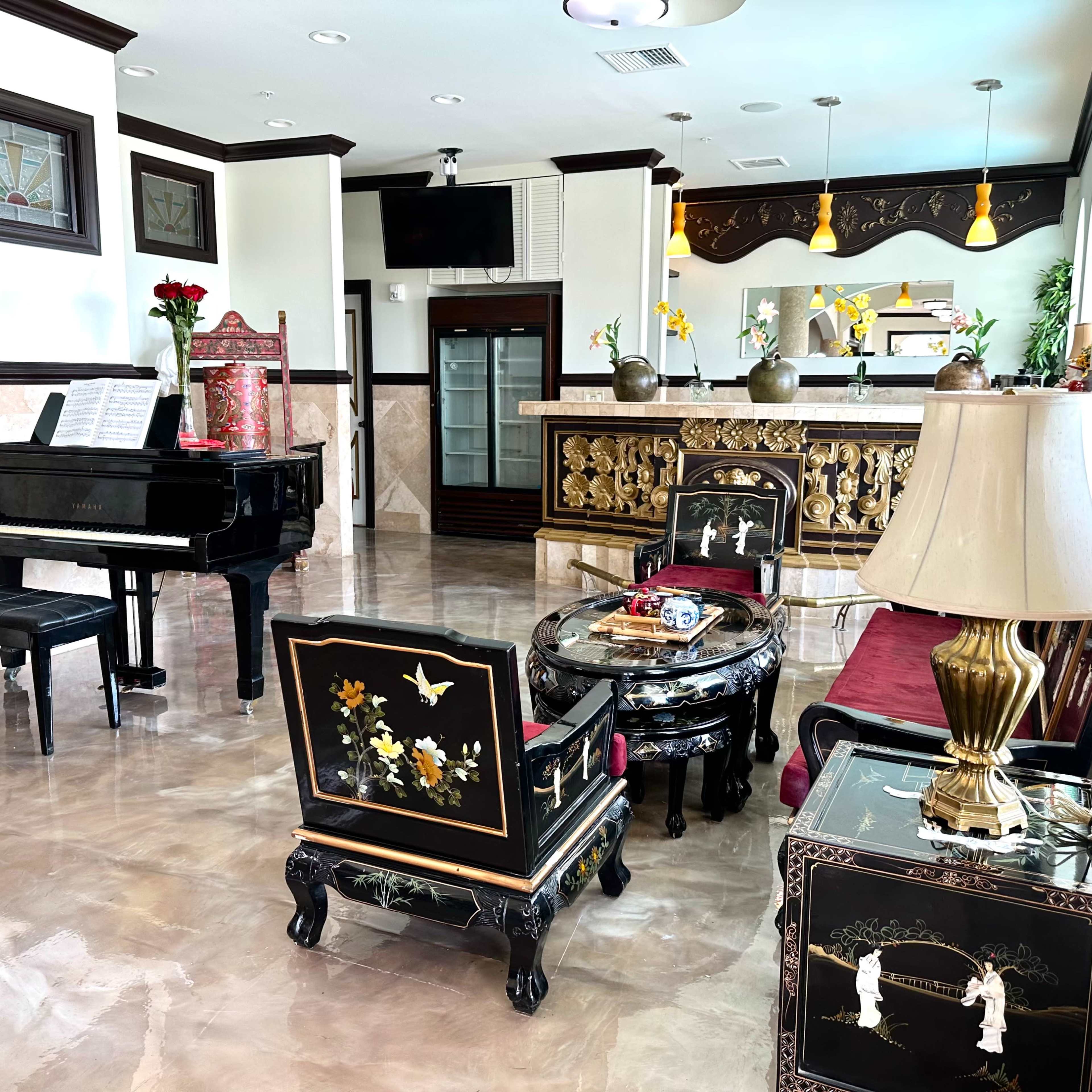 A spacious, elegantly furnished lounge area featuring a piano, a bar, and ornate seating arrangements.
