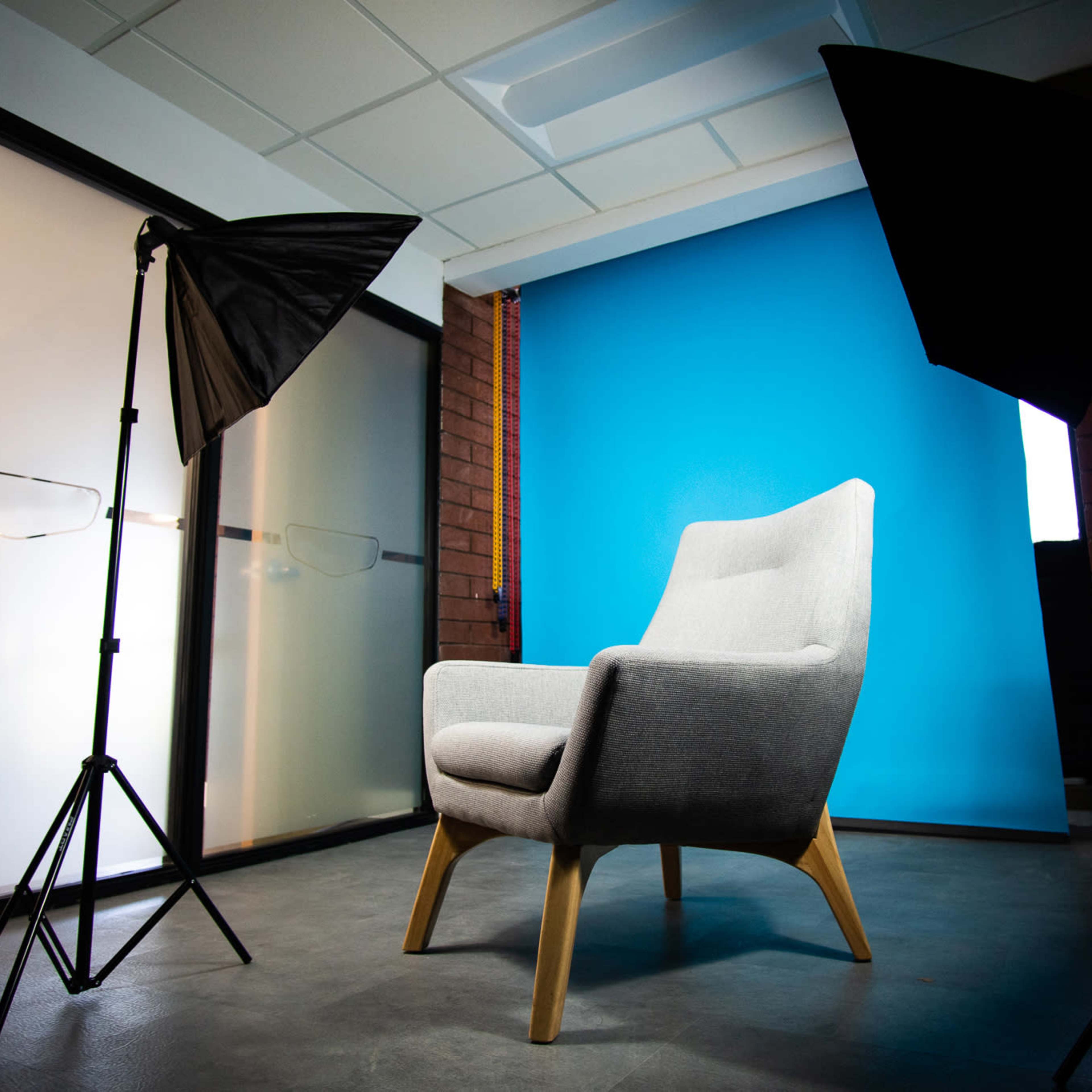 A gray armchair positioned in front of a bright blue backdrop, with two softbox studio lights on either side.