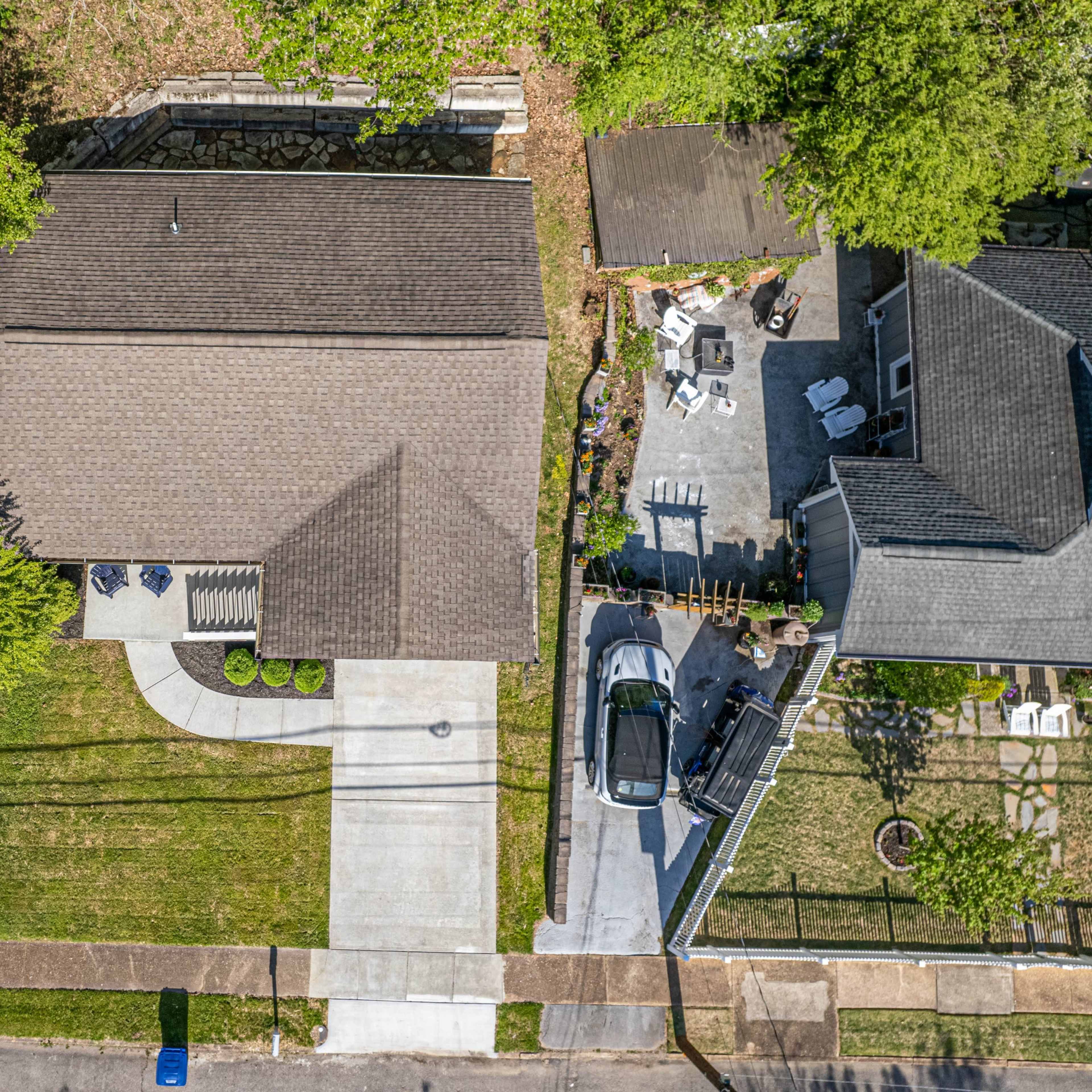 An aerial view shows a residential neighborhood featuring a single-story house with a driveway and well-maintained lawns.