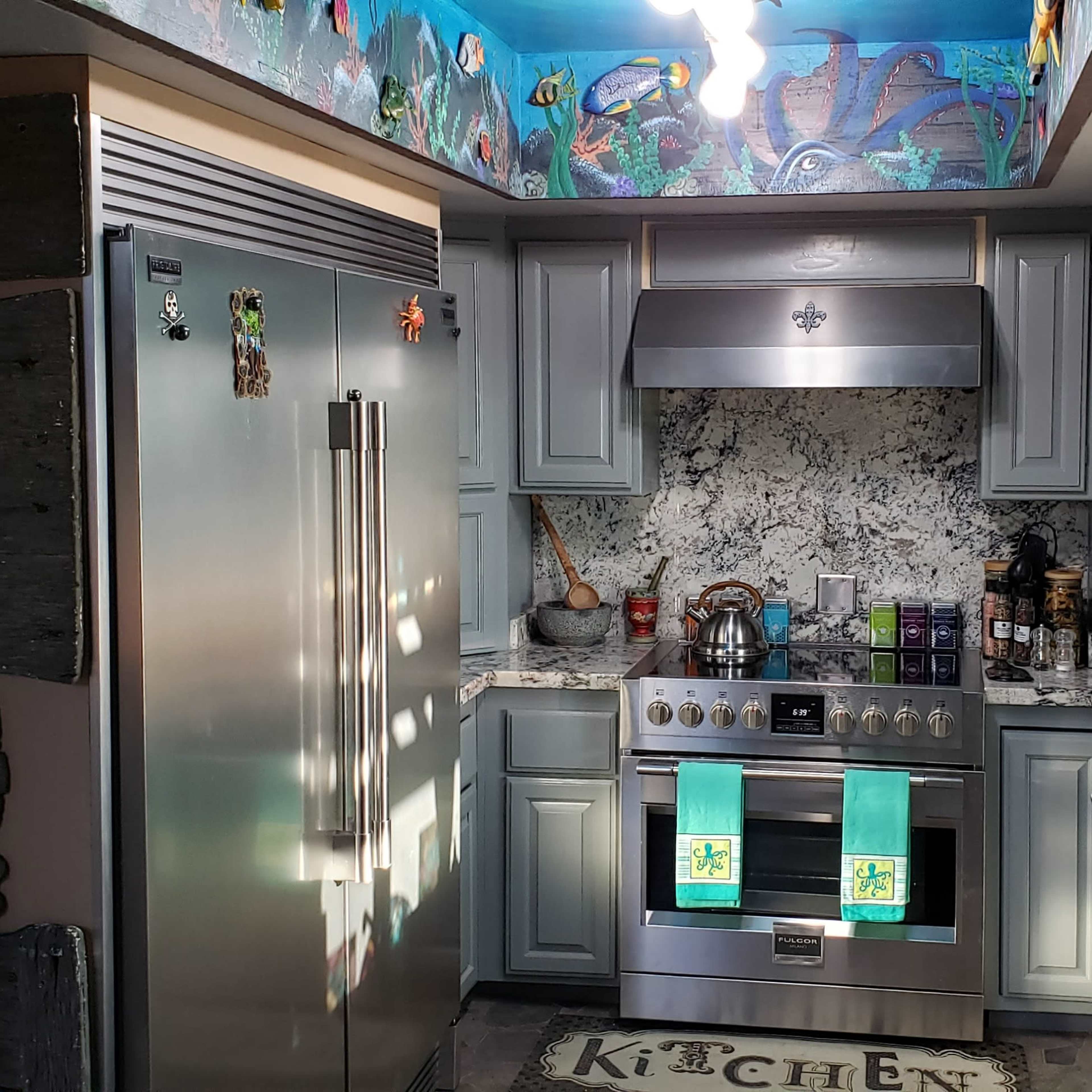 The kitchen features stainless steel appliances, gray cabinets, and a colorful mural on the ceiling depicting marine life.