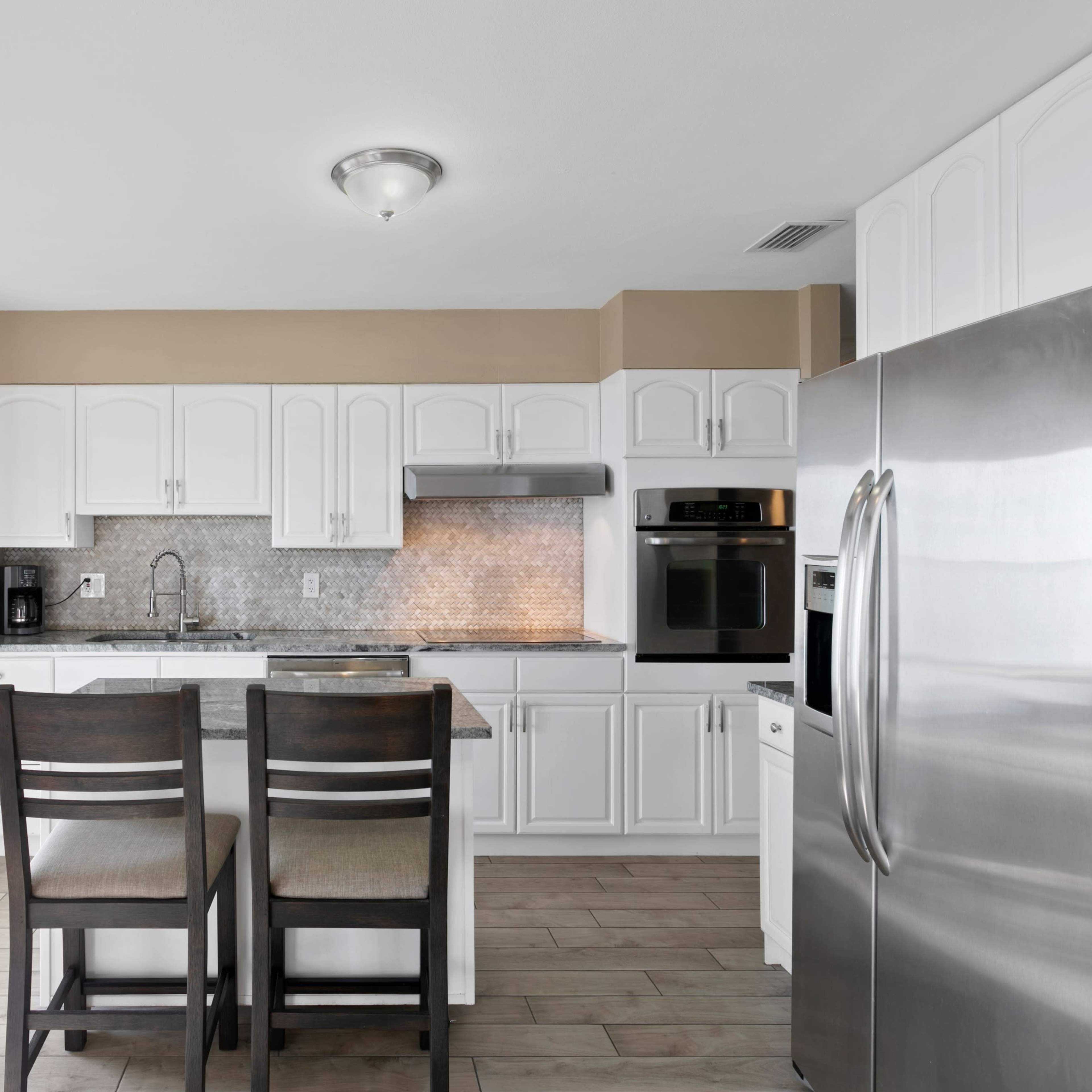 A modern kitchen features white cabinets, stainless steel appliances, and a gray tiled backsplash, with a view of the outdoors through a glass door.