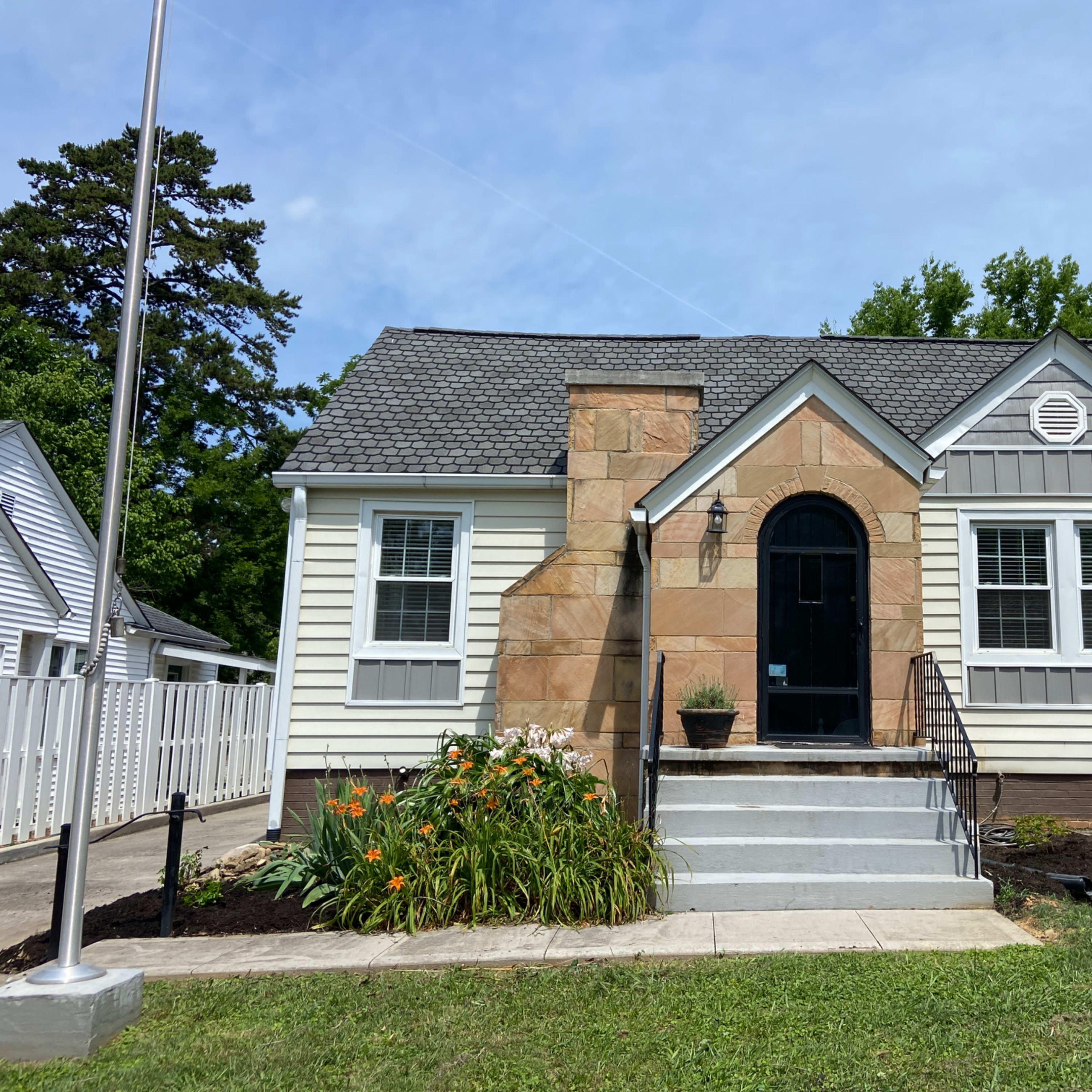 A single-story house with a stone accent wall, gray shingles, and a small front garden.