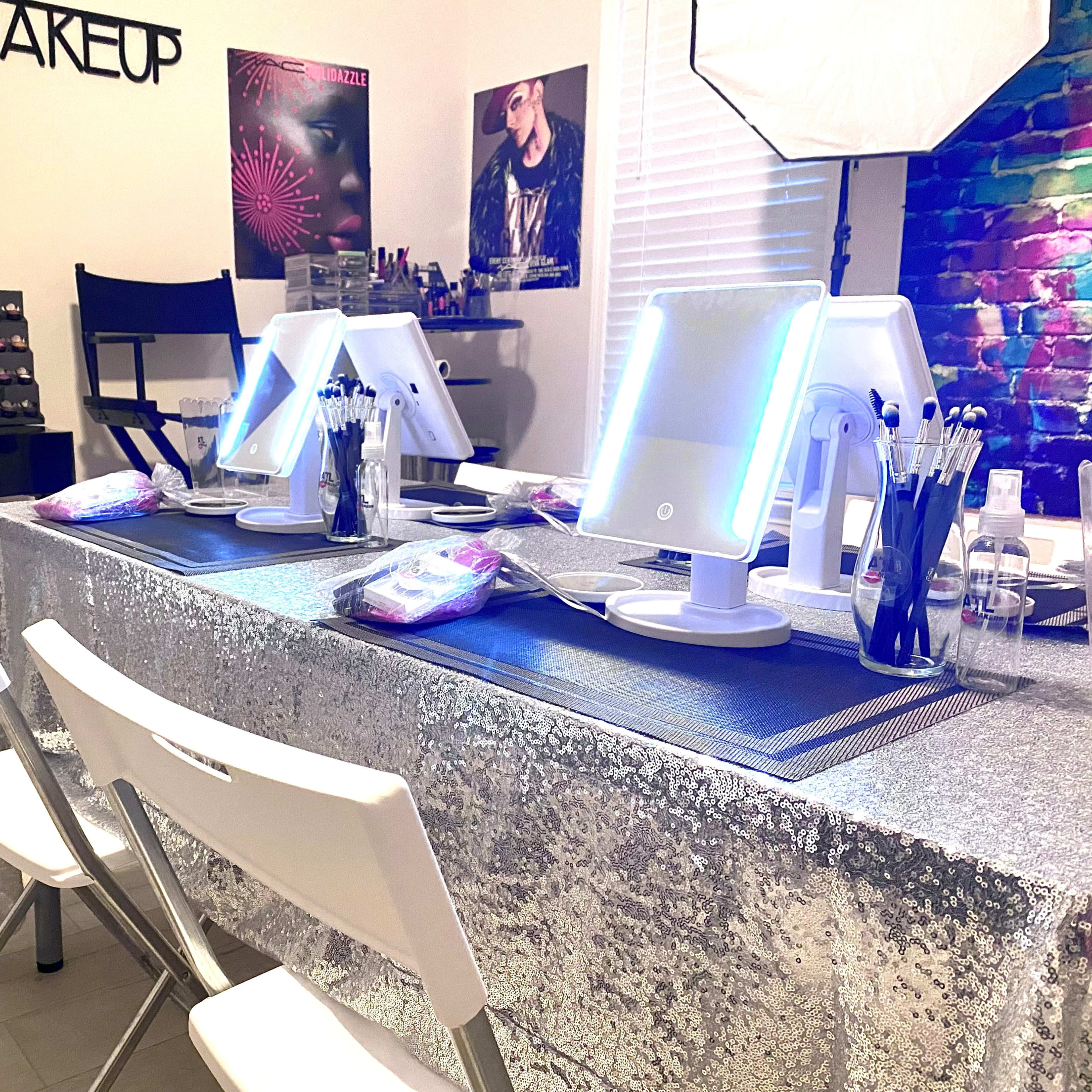 A makeup studio features a sparkling table with illuminated mirrors and organized makeup tools, surrounded by folding chairs.