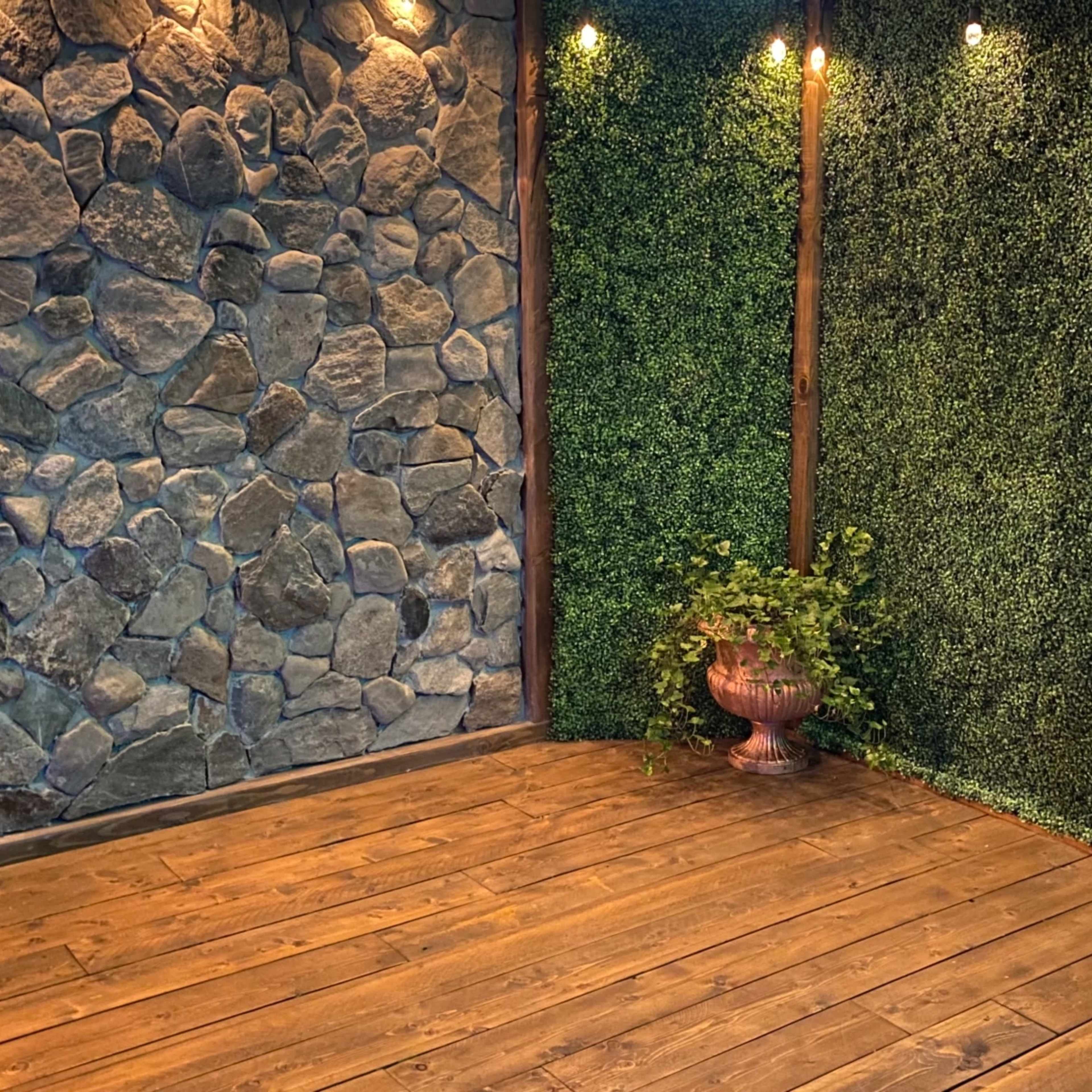 A cozy corner with a stone wall on one side and a textured green wall on the other, complemented by wooden flooring and a decorative plant in a pot.