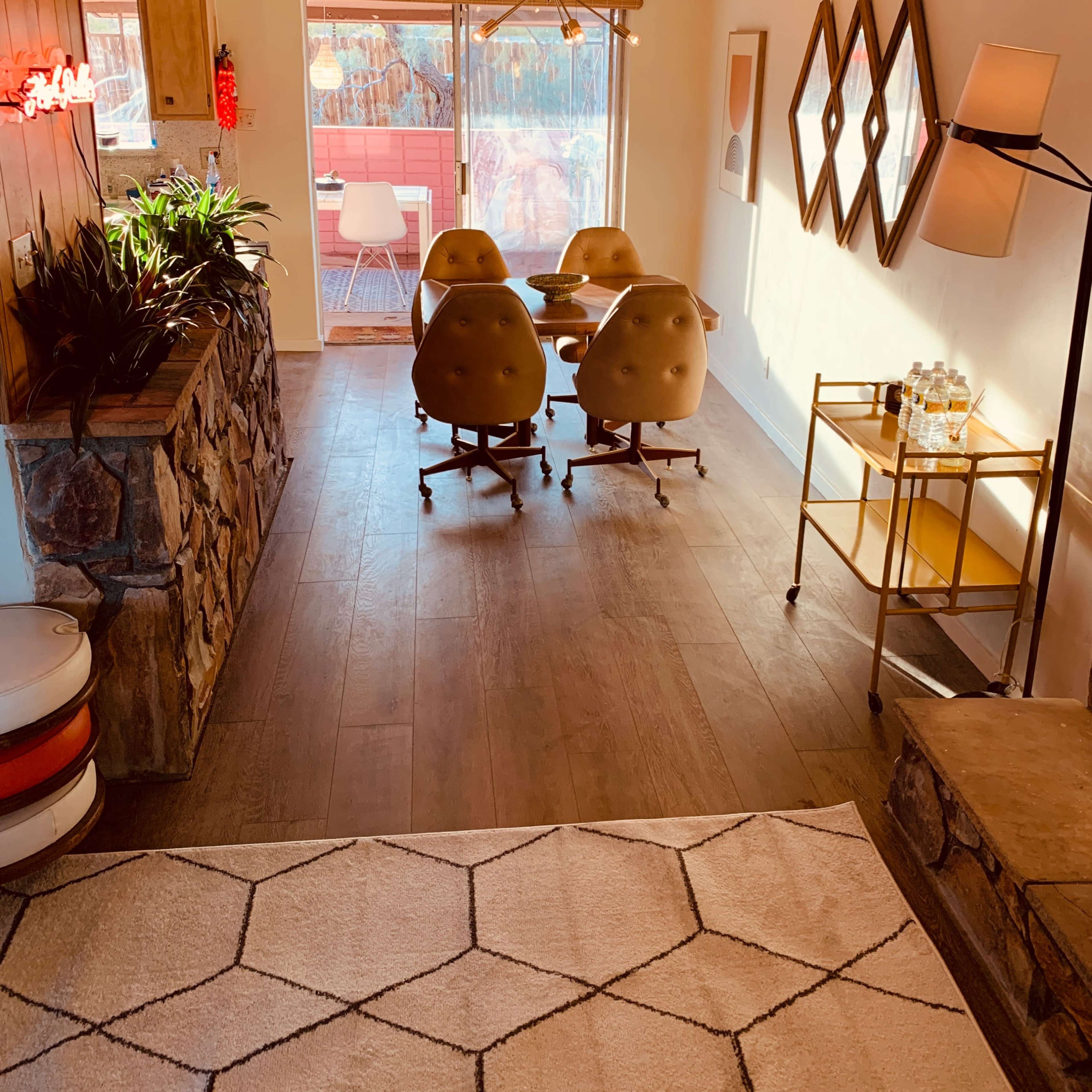 A modern dining area features a glass table with round, brown chairs, surrounded by wood-paneled walls and large windows overlooking a patio.