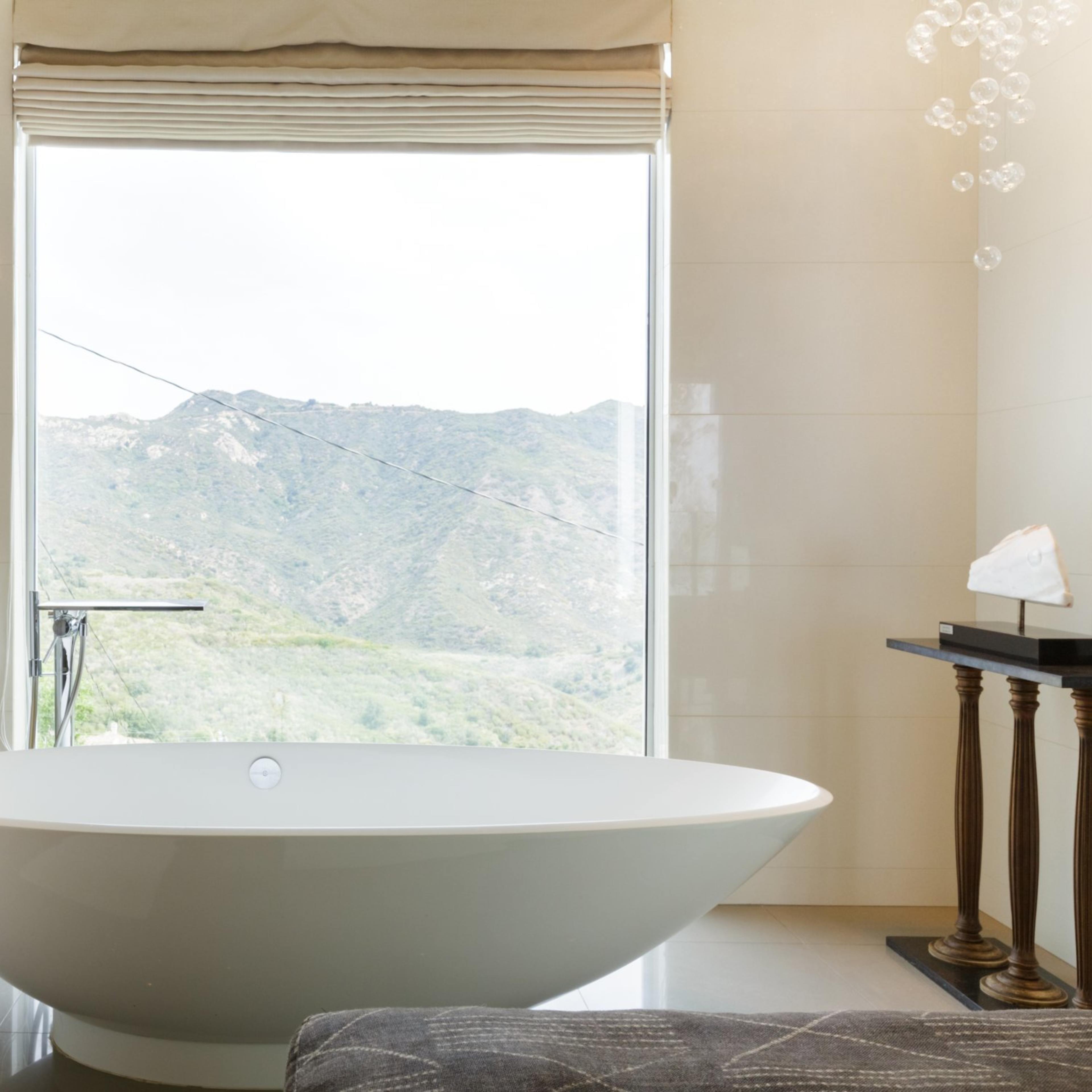 A freestanding bathtub is positioned in front of a large window that offers a view of a mountain landscape.