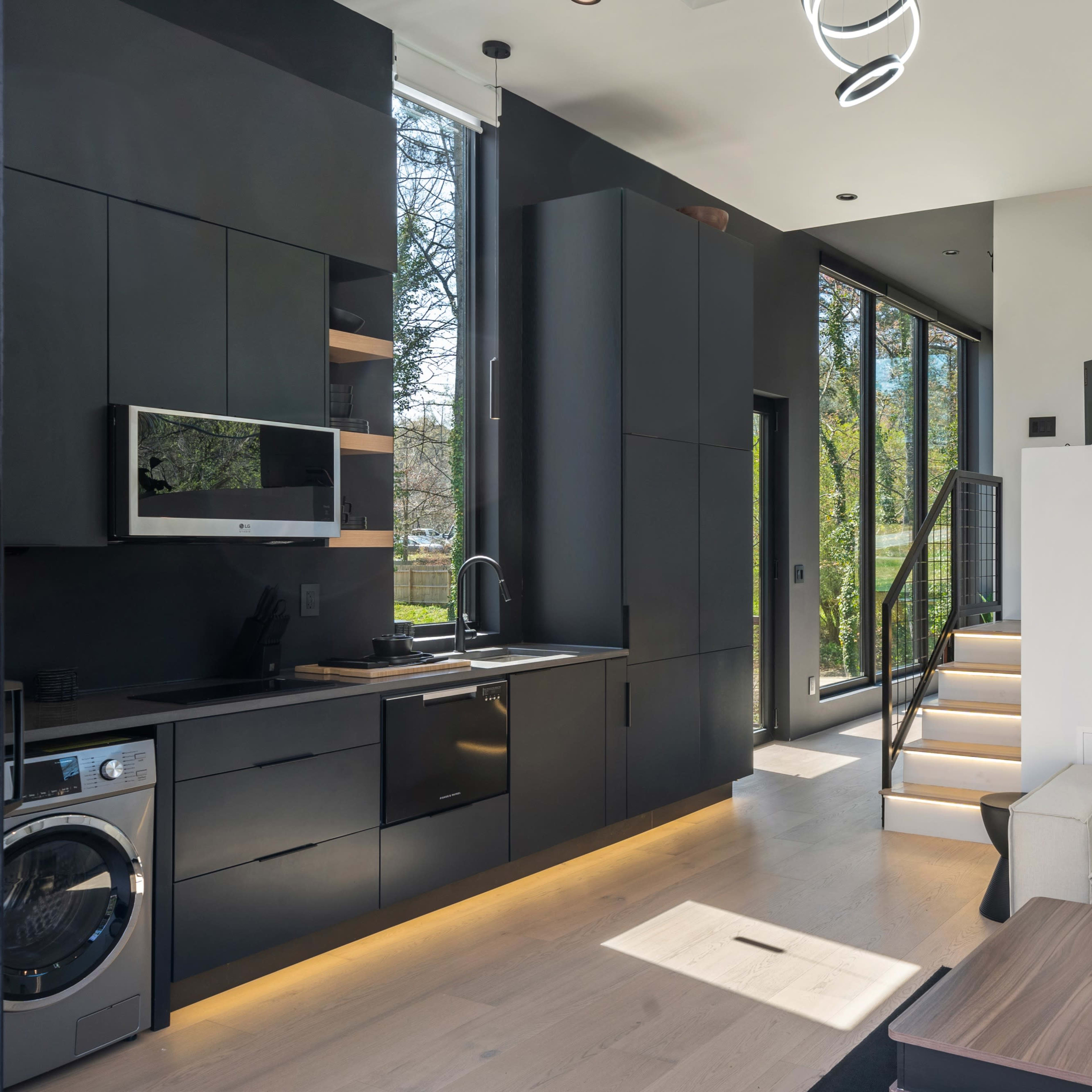 A modern living space featuring a black kitchen, a light-toned sofa, and large windows allowing natural light to fill the room.