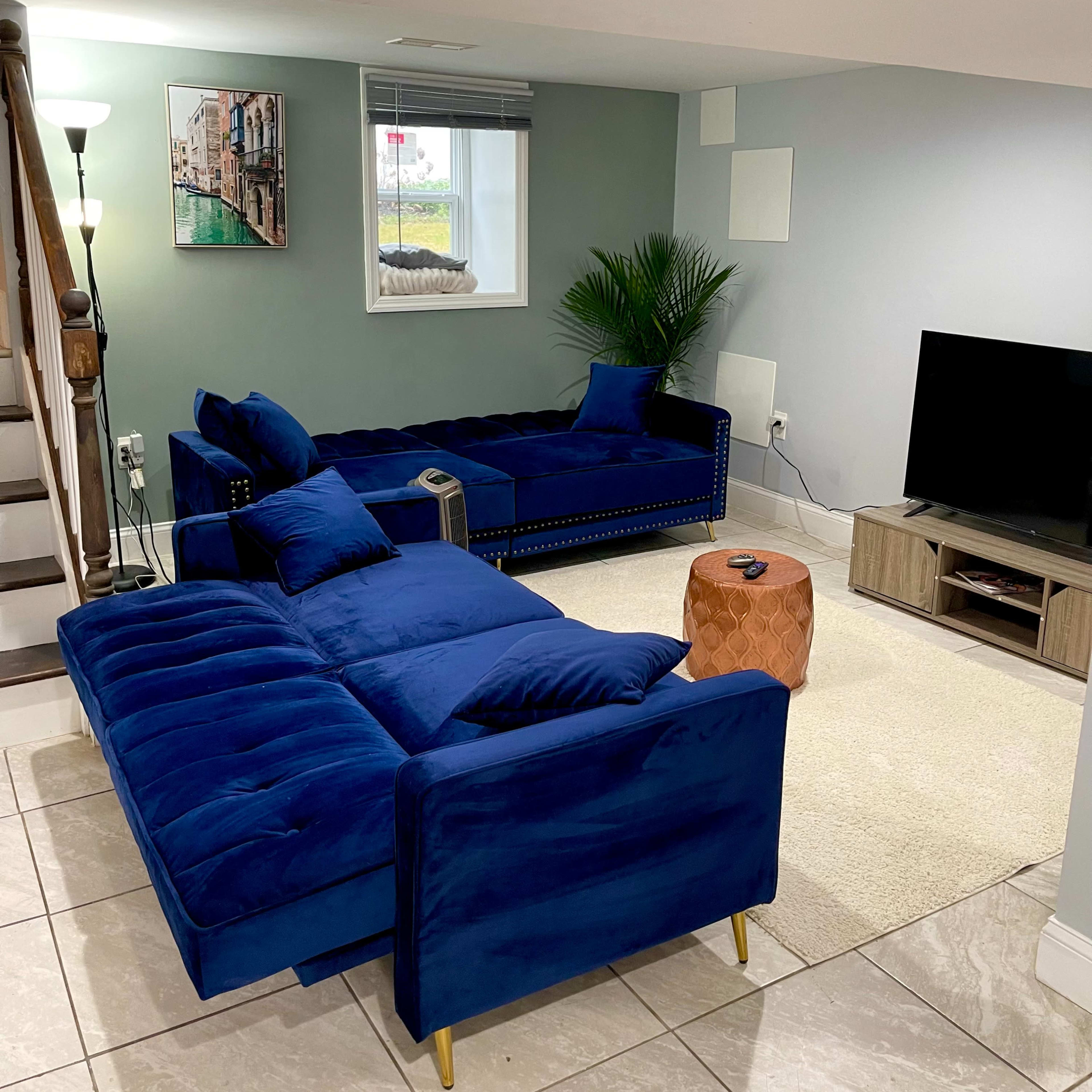 A modern living room featuring a blue sectional sofa, a wooden TV stand, and a small side table on a tile floor.