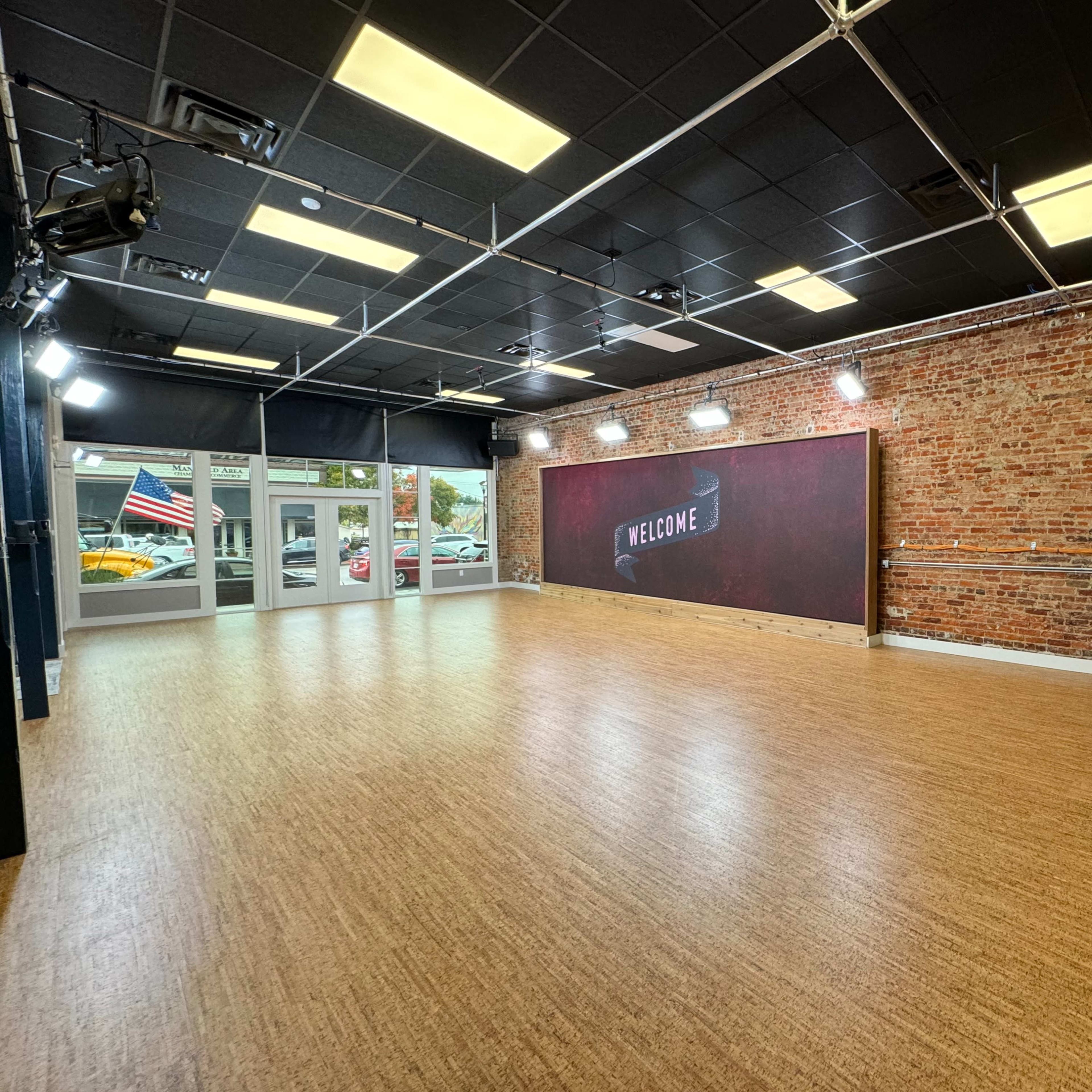 A spacious, empty room with a brick wall and a large "WELCOME" sign, illuminated by overhead lights.