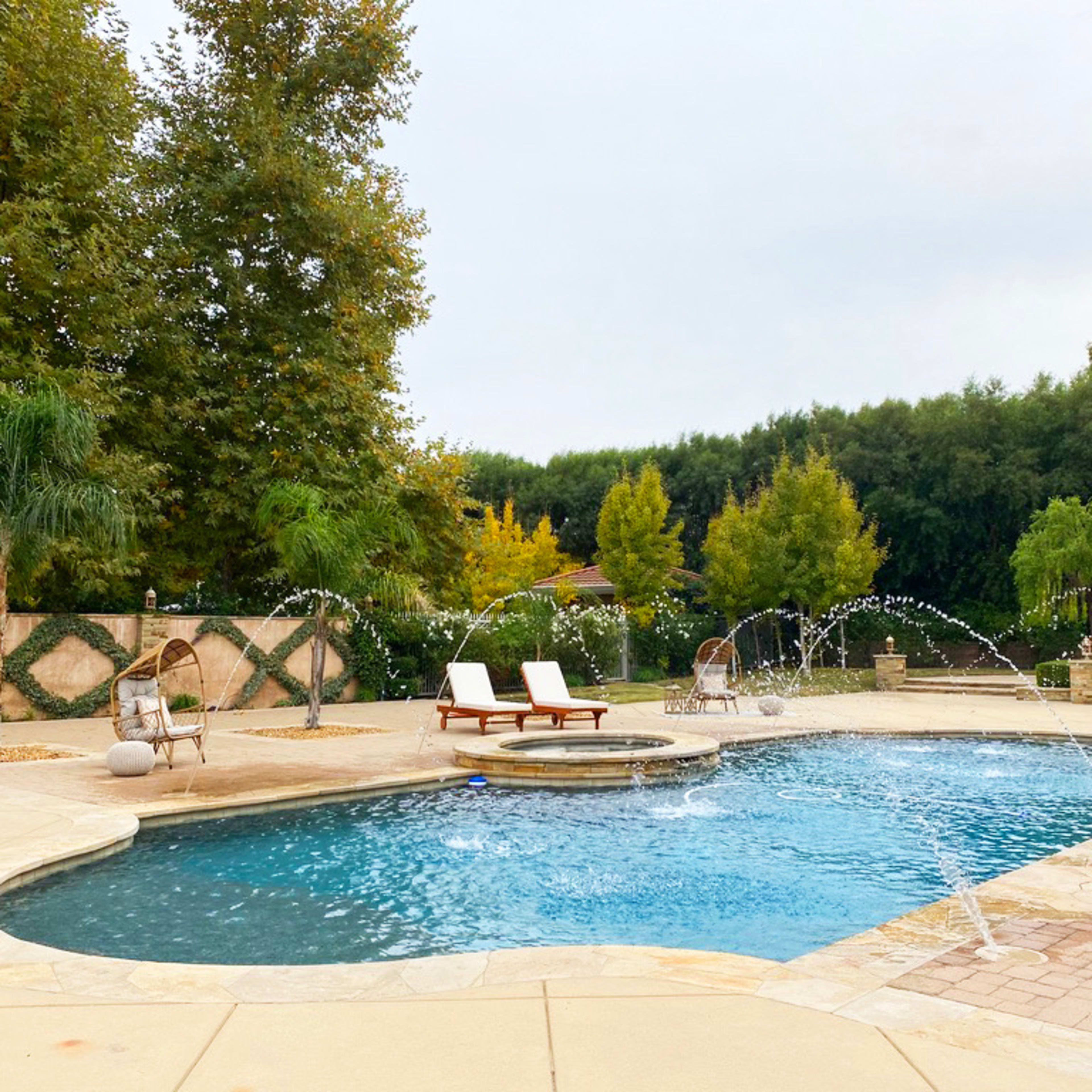 A swimming pool with a spa area features water fountains, surrounded by lounge chairs and landscaped greenery.