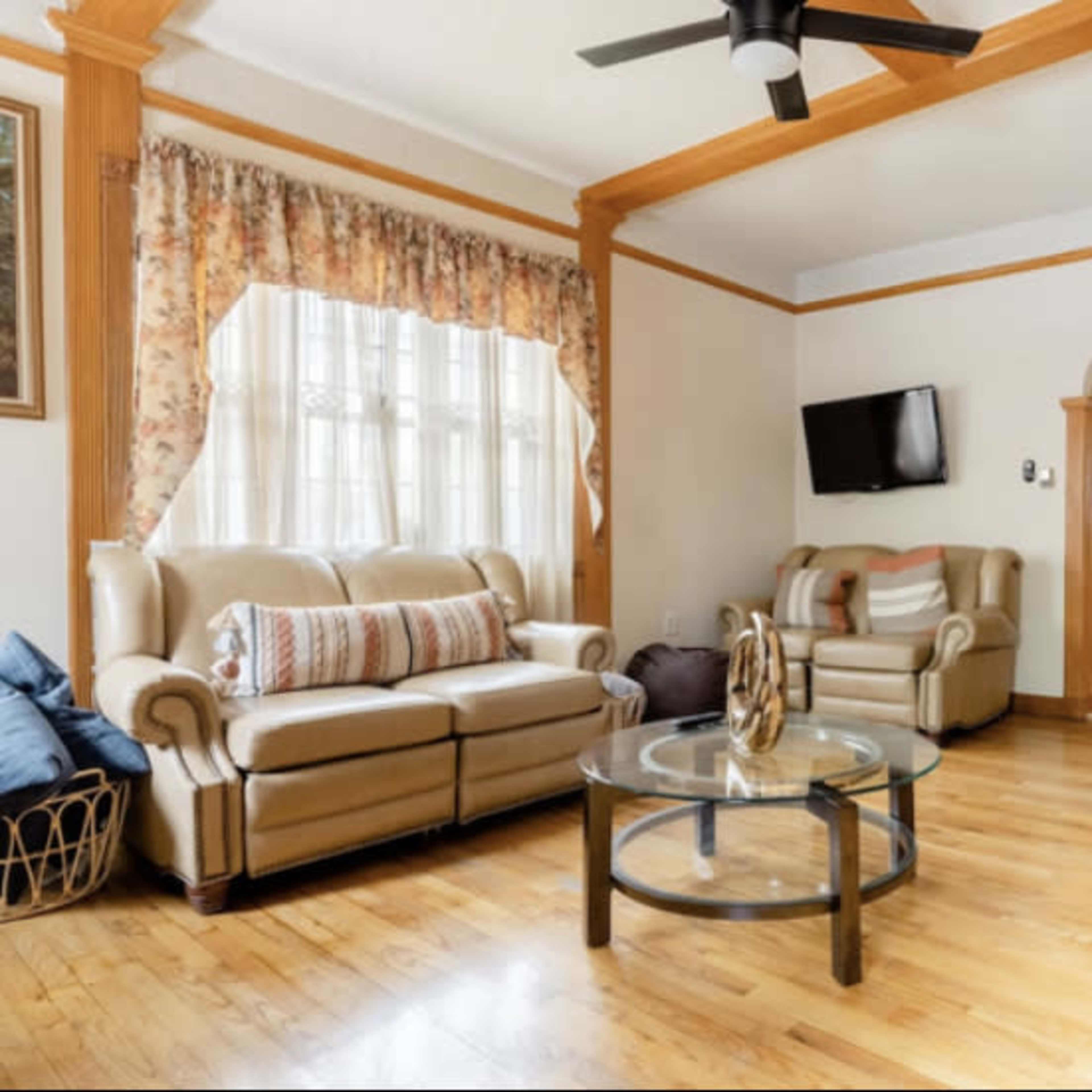 A living room with two beige sofas, a glass coffee table, and a television mounted on the wall, all set on a wooden floor.