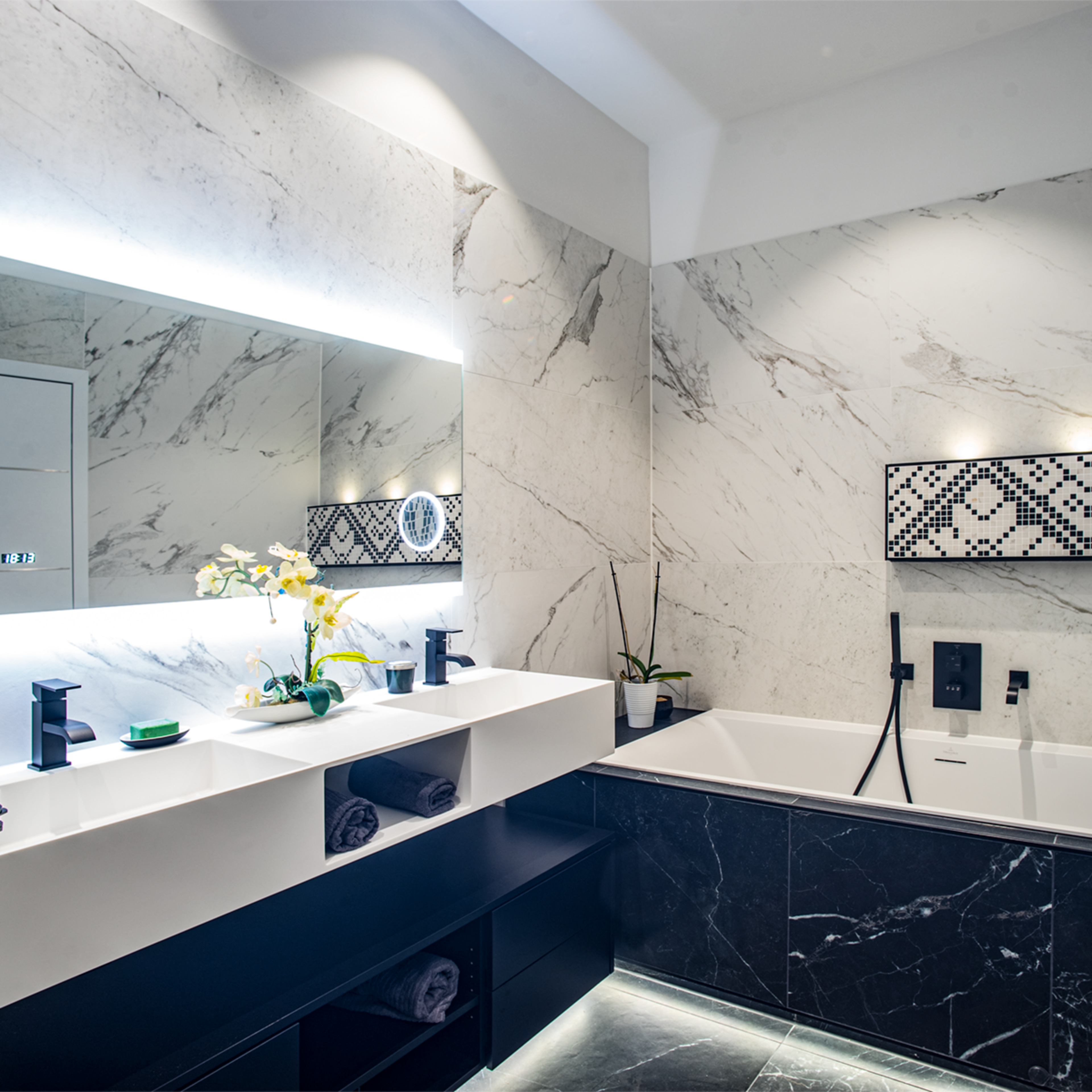 A modern bathroom features a marble-tiled wall, a double sink vanity with a large mirror, and a freestanding bathtub.
