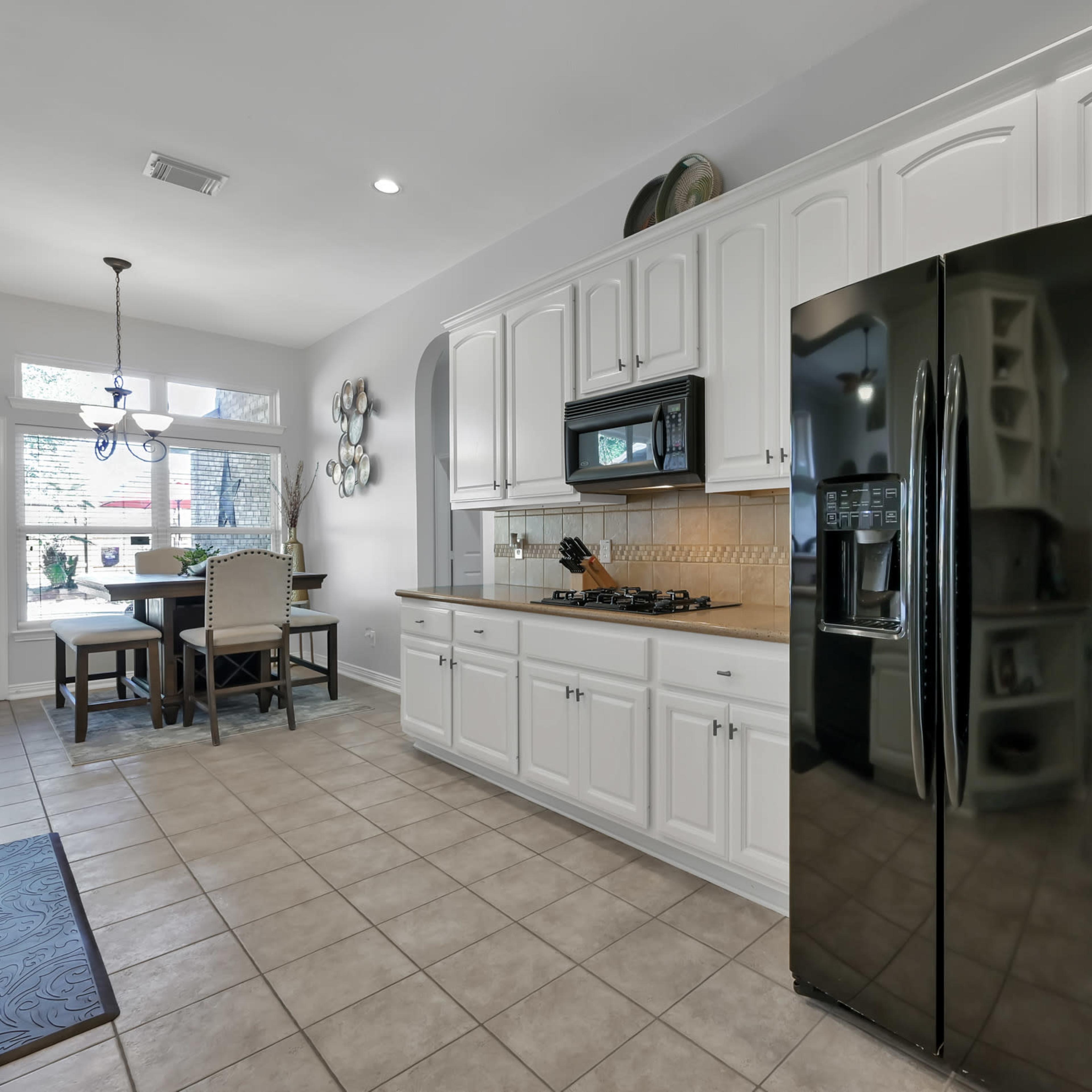A modern kitchen with white cabinets, a black refrigerator, and a dining area featuring a table and chairs.