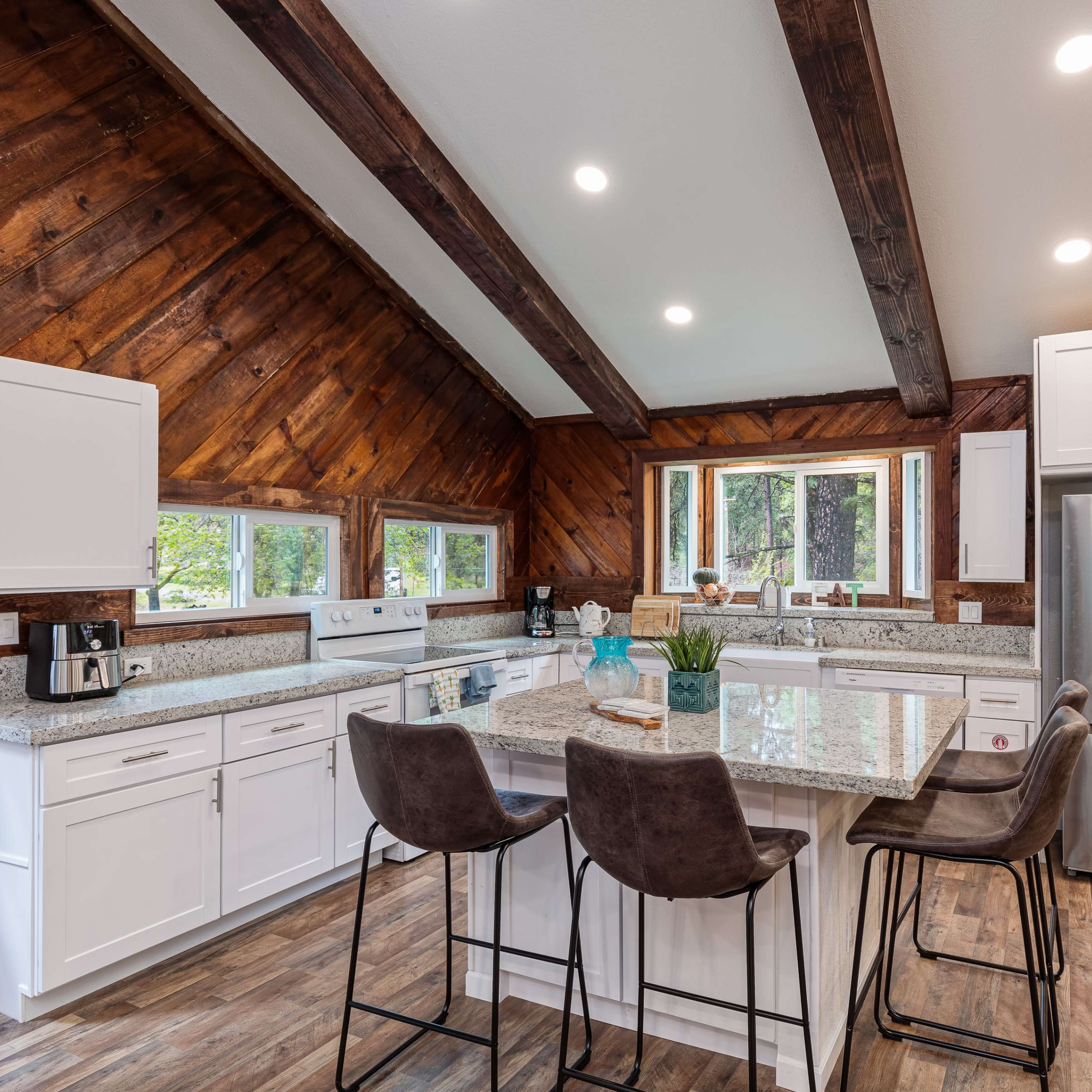 A modern kitchen with a large island, white cabinetry, stainless steel appliances, and wood-paneled vaulted ceilings.
